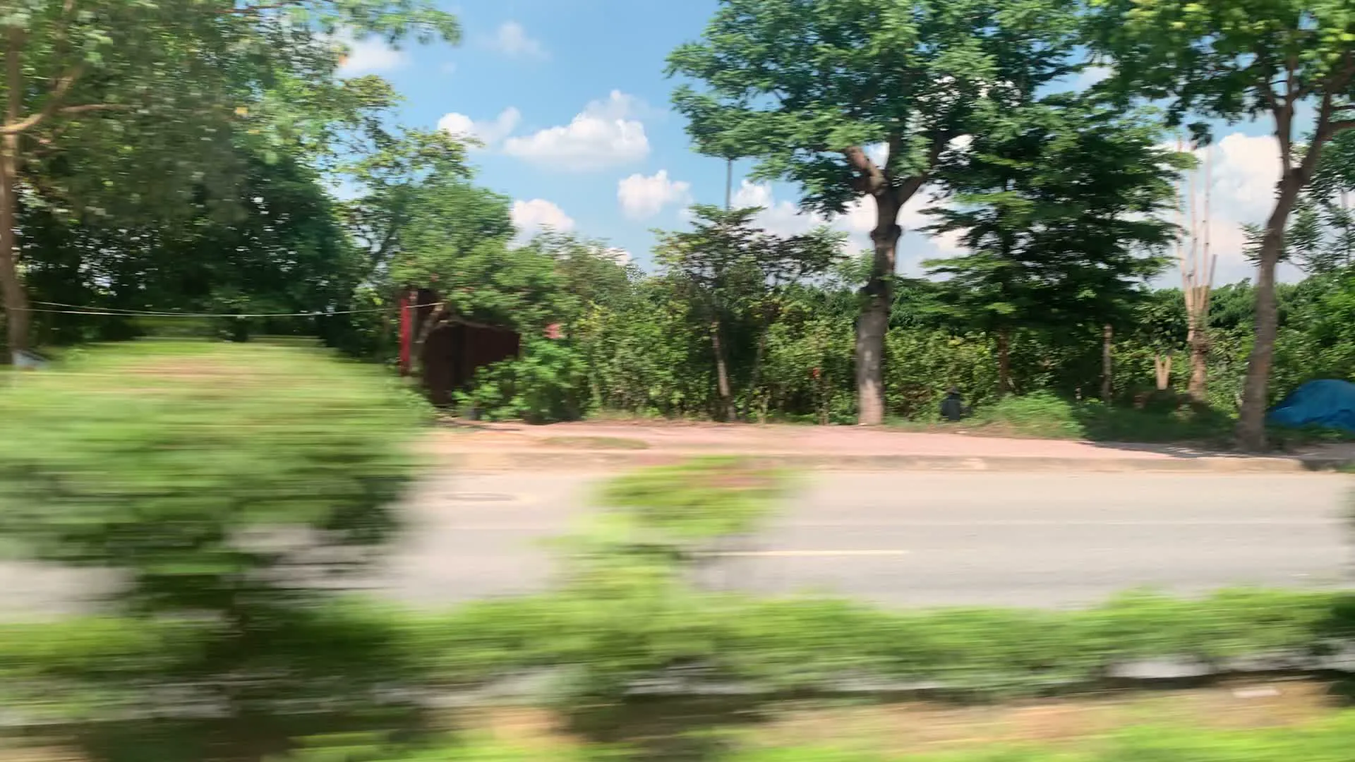 Video được quay từ một phương tiện đang di chuyển, ghi lại cảnh quan hai bên một con đường ở khu vực ngoại thành. Khung cảnh cho thấy một con đường nhựa với nhiều cây xanh và các cửa hàng, xưởng kinh doanh san sát nhau. Bầu trời trong xanh, có mây trắng.。Các thông tin văn bản có thể nhận dạng từ các biển hiệu bao gồm:。- Biển quảng cáo màu đỏ: 'CHO THUÊ NHÀ, XƯỞNG, ĐT liên hệ: 088.65.88888'.。- Biển hiệu của một cơ sở kinh doanh: 'Hyundai Sơn Tây'.。- Biển hiệu của một xưởng sản xuất: 'XƯỞNG NHÔM ĐỨC THỊNH', chuyên về 'CỬA NHÔM ĐÚC, HÀNG RÀO, BAN CÔNG, BÀN GHẾ NHÔM ĐÚC, XÍCH ĐU, CẦU THANG'.。- Một cửa hàng lớn có tên 'LOAN TUYẾT' với biển hiệu 'YOKOHAMA', là 'NHÀ PHÂN PHỐI LỐP Ô TÔ - ẮC QUY' và 'PHÂN PHỐI ỦY QUYỀN DẦU NHỚT YOKOHAMA'. Tên công ty là 'CÔNG TY TNHH THƯƠNG MẠI DỊCH VỤ VÀ VẬN TẢI LOAN TUYẾT'.。- Các biển quảng cáo dầu nhớt 'ENEOS MOTOR OIL', trong đó có một biển ghi 'ĐẠI LÝ DẦU NHỚT ENEOS VÙNG TÂY BẮC'.。- Một biển hiệu khác quảng cáo lốp ô tô: 'LỐP Ô TÔ BMWYOTO.NET'.。Hoạt động chính được ghi lại là di chuyển bằng phương tiện giao thông trên đường. Các cửa hàng và xưởng dường như đang trong giờ hoạt động kinh doanh.