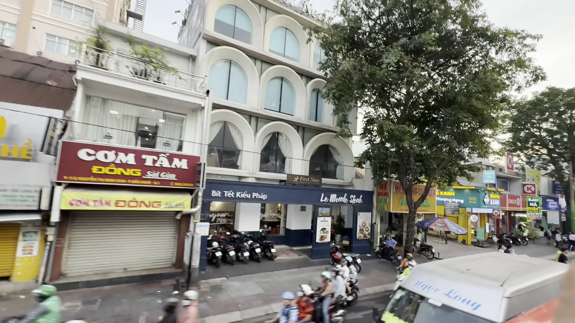 CƠM TẤM ĐÔNG Sài Gòn（コムタム・ドン・サイゴン - 砕き米定食のレストラン）。Le Monde Steak / Bít Tết Kiểu Pháp（ル・モンド・ステーキ / フランス風ビーフステーキ - ステーキレストラン）。Circle K（サークルK - コンビニエンスストア）。Pharmacity / Tiết kiệm hơn - Sống khỏe hơn（ファーマシティ / もっと節約、もっと健康に - ドラッグストアとそのスローガン）。VĂN PHÒNG PHẨM TÂN TIẾN（ヴァン・フォン・ファム・タン・ティエン - タン・ティエン文房具店）。RAU MÁ（ラウマー - ツボクサジュースのスタンド）。BOBAPOP TEA BAR（ボバポップ・ティーバー - タピオカティーのチェーン店）。MỸ PHẨM NHẬP KHẨU / NHÂN SÂM - LINH CHI（ミー・ファム・ニャップ・カウ / ニャン・サム - リン・チー - 輸入化粧品 / 高麗人参・霊芝の店）。Cơm tấm Cali（コムタム・カリ - 砕き米定食のチェーンレストラン）。HỦ TIẾU NAM VANG（フーティウ・ナムヴァン - プノンペン風米麺の看板）