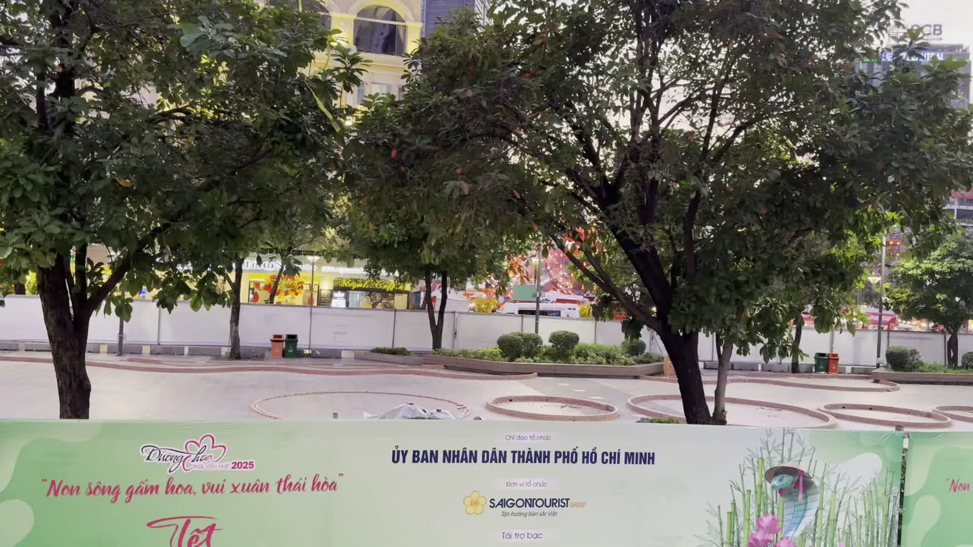 ỦY BAN NHÂN DÂN THÀNH PHỐ HỒ CHÍ MINH（ホーチミン市人民委員会 - イベントの主催指導機関として記載）。Đường hoa Nguyễn Huệ 2025（グエンフエ・フラワーロード 2025 - ホーチミン市のグエンフエ通りで毎年テトに開催されるフラワーフェスティバルの名称）。"Non sông gấm vóc, vui xuân thái hòa"（錦の如き祖国、平和な春を楽しむ - イベントのスローガン）。Saigontourist Group（サイゴンツーリスト・グループ - イベントの主催団体）。GPS座標からREX HOTEL SAIGONの一部と推定される）