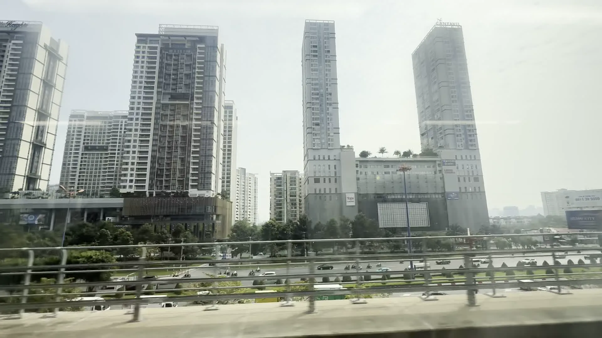 Cantavil Premier（カンタビル・プレミア、ホーチミン市トゥードゥック市の高層複合施設）。The Estella Heights（ジ・エステラ・ハイツ、ホーチミン市トゥードゥック市の高級マンション・商業複合施設）。PwC（プライスウォーターハウスクーパース、エステラ・ハイツに入居する企業のロゴ）。MEKONGADS（メコンアズ、看板に記載された広告会社名）。Tuyến metro số 1 Bến Thành - Suối Tiên（ベンタイン-スオイティエン メトロ1号線、車窓から撮影された高架鉄道）