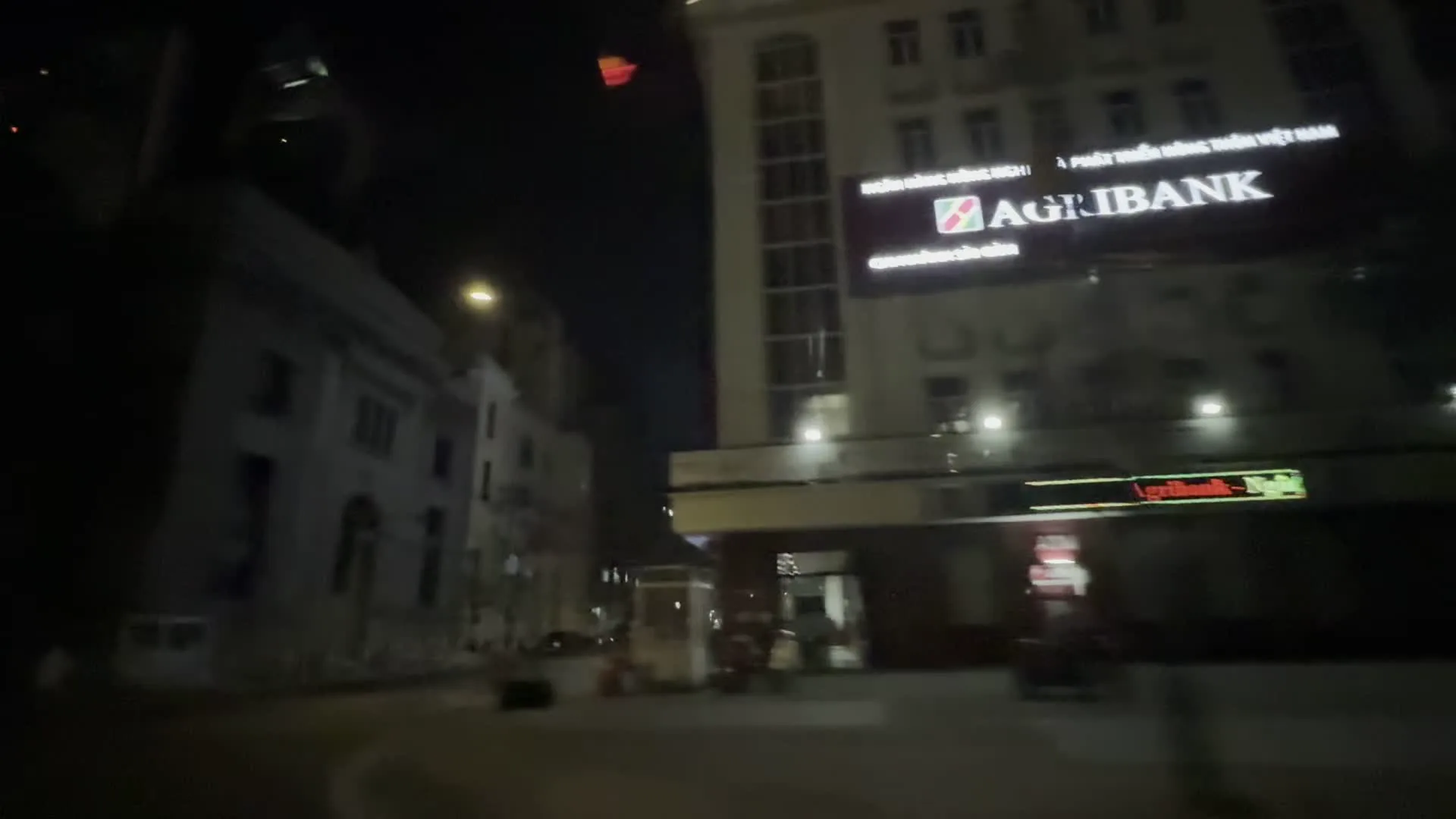 Cảnh quay được thực hiện vào ban đêm trên một con đường trong thành phố, nhìn từ một phương tiện đang di chuyển. Hình ảnh cho thấy các tòa nhà, đèn đường và một vài phương tiện giao thông khác. Do phương tiện di chuyển nhanh nên một số hình ảnh bị mờ. Có thể nhận diện được các biển hiệu của ngân hàng. Một tòa nhà lớn có biển hiệu màu đỏ và trắng ghi rõ "AGRIBANK". Phía trên logo có vẻ như là dòng chữ "Ngân hàng Nông nghiệp và Phát triển Nông thôn Việt Nam". Phía trước tòa nhà có một bốt bảo vệ. Một tòa nhà khác có biển hiệu phát sáng của "VietinBank". Quang cảnh cho thấy một đường phố đô thị vào buổi tối.