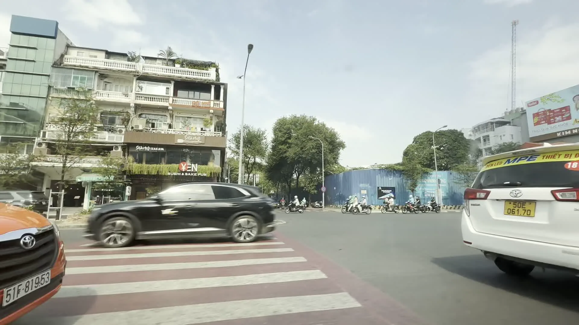 YEN Sushi & Sake Pub（イェン寿司＆酒パブ）。SUSHI DAN（寿司DAN - 日本食レストラン）。FAHASA（ファハサ - ベトナムの書店チェーン）。EL GAUCHO（エル・ガウチョ - アルゼンチンステーキハウス）。LIBERTY CENTRAL（リバティセントラル - ホテル）。TISSOT（ティソ - スイスの時計ブランド）。KFC（KFC - ファストフードチェーン）。TAN TAN（タンタン - 店舗名）。ABBank（アンビン銀行）。INAMO（イナモ - レストラン）。The Alley（ジ・アレイ - 飲料店）。MOMO（モモ - 電子決済サービス）。MPE THIẾT BỊ ĐIỆN（MPE電設資材 - タクシー広告）。50E - 061.70（ホーチミン市の車両ナンバープレート）。51F - 819.53（ホーチミン市の車両ナンバープレート）