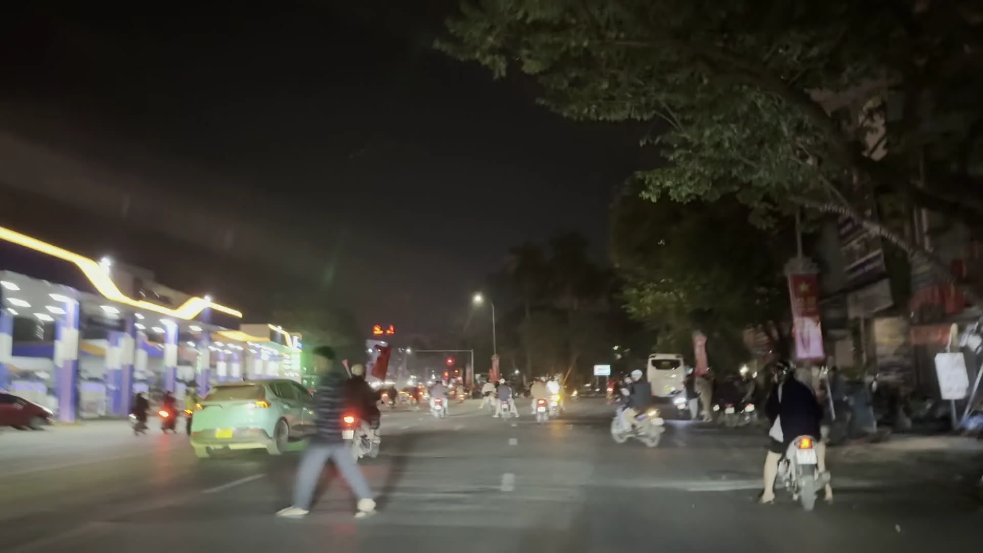 Khung cảnh đường phố Hà Nội về đêm, có một đoàn người rất đông đang diễu hành bằng xe máy. Hoạt động này thường được gọi là "đi bão", có thể là để ăn mừng một chiến thắng thể thao. Nhiều người cầm cờ đỏ sao vàng của Việt Nam, một số người còn khoác cờ lên người. Trong đoàn xe có nhiều xe máy, một vài ô tô và một chiếc xe tải màu trắng có dòng chữ "JS COOLTRANS". Dọc hai bên đường là cây xanh, các tòa nhà, một trạm xăng đang sáng đèn và có thể nhìn thấy một biển hiệu màu đỏ ghi chữ "KOME LIFE".