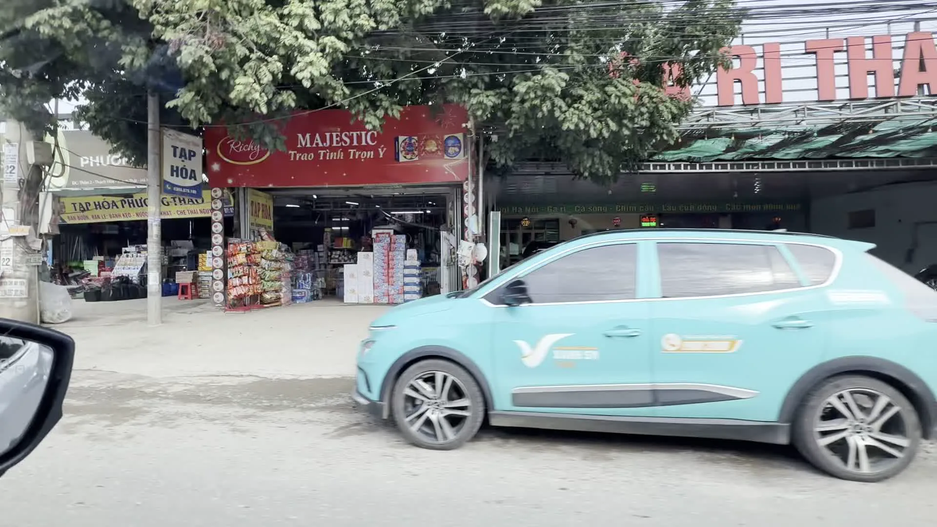 Tạp hóa（雑貨店）。Nhà hàng Bê Chao Tây Bắc, chuyên về ẩm thực Tây Bắc（タイバック風仔牛の炙り焼きレストラン、タイバック料理専門店の看板）。Gà tươi Mạnh Hoạch（マンホアック・ブランドの新鮮な鶏肉の看板）。Địa chỉ: Thôn 2, Thạch Hoà, Thạch Thất, Hà Nội（住所表記：ハノイ市タックタット県タックホア社第2村）。Nhà nghỉ（簡易宿泊所）