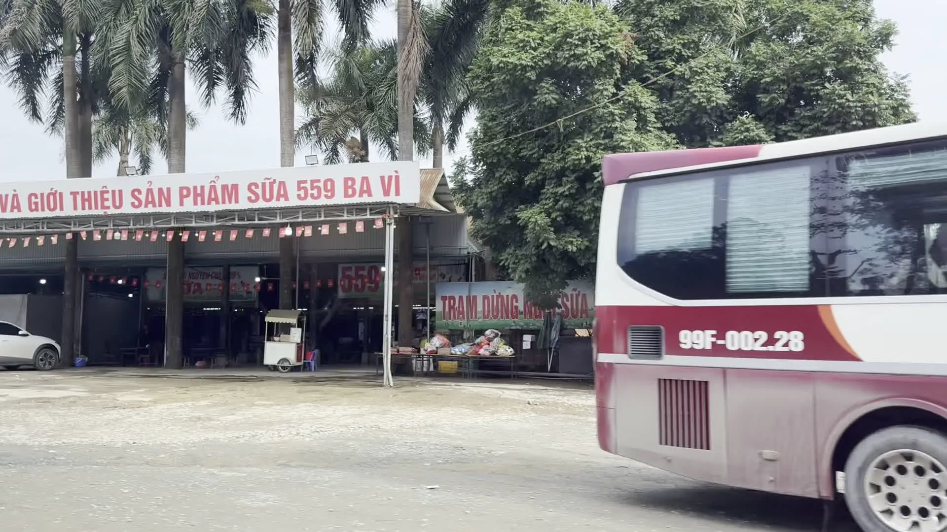 GIỚI THIỆU SẢN PHẨM SỮA 559 BA VÌ（バーヴィー559乳製品紹介の看板。バーヴィーは乳製品で有名なハノイ郊外の地名）。TRẠM DỪNG... SỮA（牛乳休憩所の看板）。BIA TƯƠI HÀ NỘI（ハノイ生ビールの看板）。THẢO DƯỢC QUÁN（薬草の店の看板）。BÁN ĐẤT（「土地売ります」の看板）。99F-002.28（バスのナンバープレート。99はバクニン省の登録コード）