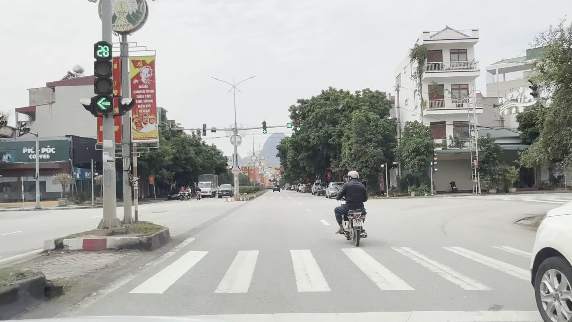 Đường Trần Hưng Đạo, thành phố Hòa Bình (ホアビン市、チャン・フン・ダオ通り)。Cổng chào trang trí biểu tượng tỉnh Hòa Bình (ホアビン省のシンボルが飾られた歓迎ゲート)。PIC - PỐC COFFEE (ピック・ポック・コーヒー)。Tòa nhà An Lạc Group (アンラックグループのビル)。Pano cổ động chính trị với khẩu hiệu "Đảng quang vinh - Bác Hồ vĩ đại" (「栄光ある党 - 偉大なるホーおじさん」のスローガンが書かれた政治プロパガンダのパネル)