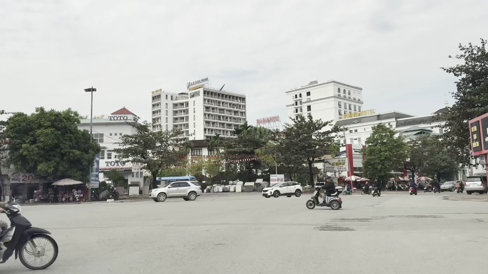 Quảng trường Hòa Bình（ホアビン広場）。SAKURA Hotel（サクラホテル）。Grand Hotel（グランドホテル）。Hoa Đào Hotel（ホアダオホテル）。TOTO（TOTO、日本の住宅設備機器メーカーの看板）。Gạch ốp lát（タイル、建材店の看板）。Bia Saigon（サイゴンビール、ベトナムのビールブランドの看板）