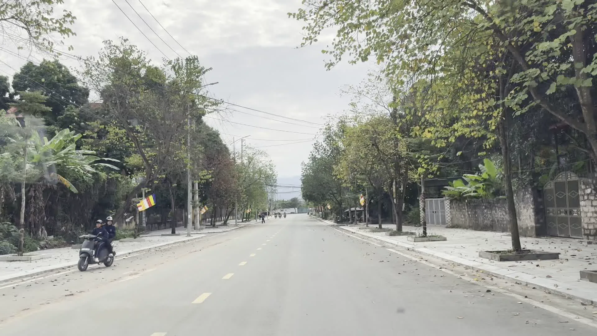 Chùm ảnh ghi lại quang cảnh trên các con đường ở một khu vực nông thôn hoặc thị trấn miền núi. Bầu trời nhiều mây.。Ảnh đầu tiên cho thấy một con đường nhựa rộng rãi và khá vắng vẻ, hai bên là hàng cây xanh và vỉa hè. Ở giữa đường có vạch kẻ màu vàng. Phía bên trái, có hai người đang đi trên một chiếc xe máy. Dọc theo con đường có treo một vài lá cờ Phật giáo màu vàng. Xa xa phía cuối con đường có thể thấy bóng vài người đang đi bộ và hình dáng của dãy núi.。Ảnh thứ hai chụp một con đường làng nhỏ hơn, có vạch kẻ sang đường. Bên phải là một dãy nhà cấp bốn nằm ngay dưới một sườn đồi rậm rạp cây cối, trước một ngôi nhà có cắm lá cờ đỏ sao vàng của Việt Nam. Một chiếc xe máy đang đỗ ven đường. Bên trái có một biển báo giao thông hình tam giác và một biển báo phụ hình chữ nhật màu xanh nhưng chữ viết trên đó không thể đọc được.。Ảnh thứ ba dường như được chụp từ trong ô tô, nhìn ra một điểm dừng chân ven đường. Có hai chiếc xe máy đang đỗ cạnh một bờ tường gạch thấp. Phía sau là khung cảnh đồi núi. Cây cối và một mái che đơn sơ cũng có thể được nhìn thấy.