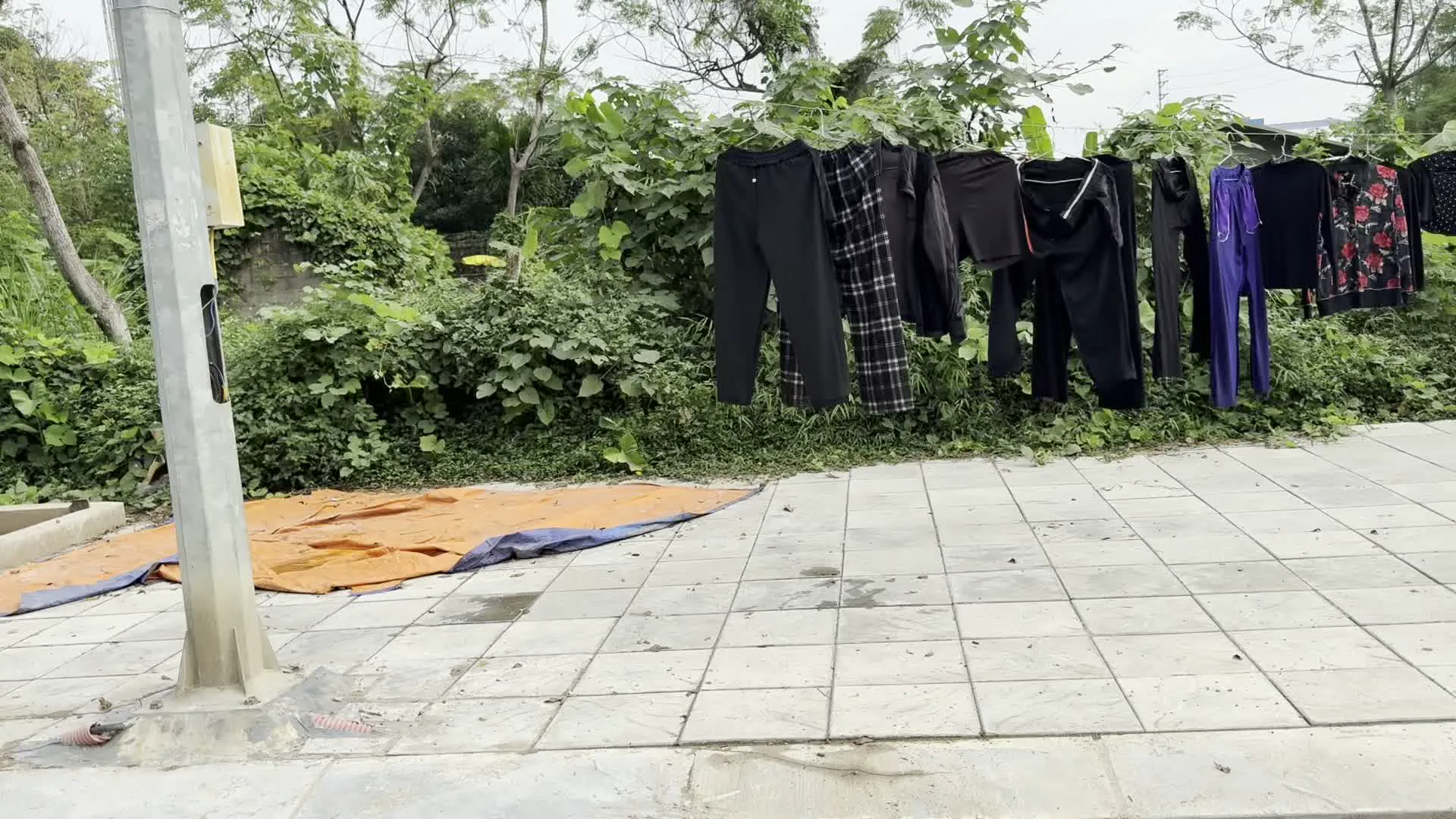 Chùm ảnh ghi lại những cảnh quan khác nhau trong một khu dân cư. Ảnh đầu tiên cho thấy quần áo, bao gồm quần dài màu đen và quần kẻ sọc, được phơi trên dây phơi căng ngang một bụi cây rậm rạp ven vỉa hè lát gạch. Dưới đất có một tấm bạt màu cam và xanh. Ảnh thứ hai là một con đường nhỏ trong khu dân cư với những ngôi nhà cao tầng màu trắng ở hai bên. Một chiếc ô tô đang ở phía xa trên đường, và một lá cờ Phật giáo được treo trên cây bên phải. Ảnh thứ ba chụp cảnh bên lề đường có vạch kẻ dành cho người đi bộ, nơi một dãy xe đẩy rác bằng kim loại được xếp dưới một gốc cây trên vỉa hè.