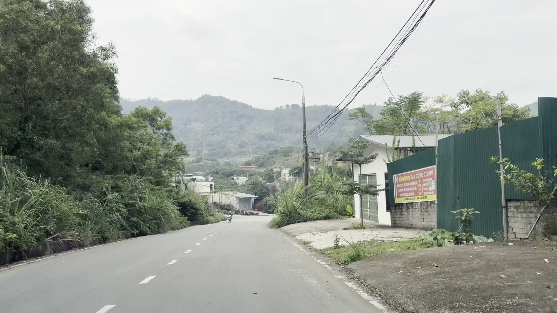 Khung cảnh cho thấy một con đường nhựa ở một vùng nông thôn miền núi. Xung quanh là những ngọn đồi xanh mướt. Hai bên đường có nhiều cây cối và cỏ dại mọc um tùm. Có một vài ngôi nhà dân nằm xen kẽ trong khu vực. Một hệ thống dây điện và cột điện chằng chịt bắc qua đường. Trong một bức ảnh, bên phải đường có một hàng rào tôn màu xanh lá cây, trên đó có treo một tấm biển quảng cáo màu đỏ với dòng chữ màu trắng và vàng "GIA CÔNG CƠ KHÍ". Các dòng chữ nhỏ hơn bên dưới không thể đọc rõ. Các bức ảnh khác chụp tại một ngã ba đường. Bầu trời có vẻ âm u.