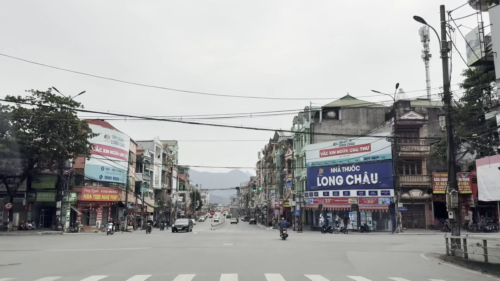NHÀ THUỐC LONG CHÂU (薬局ロンチャウ)。HỆ THỐNG HEAD HOÀI TƯƠI 1 (ホンダ正規販売店 ホアイトゥオイ1号店)。CHÚ Ý QUAN SÁT (注意して観察せよという交通安全標語)。Vòng xuyến trung tâm thành phố Hòa Bình (ホアビン市中央ラウンドアバウトとモニュメント)