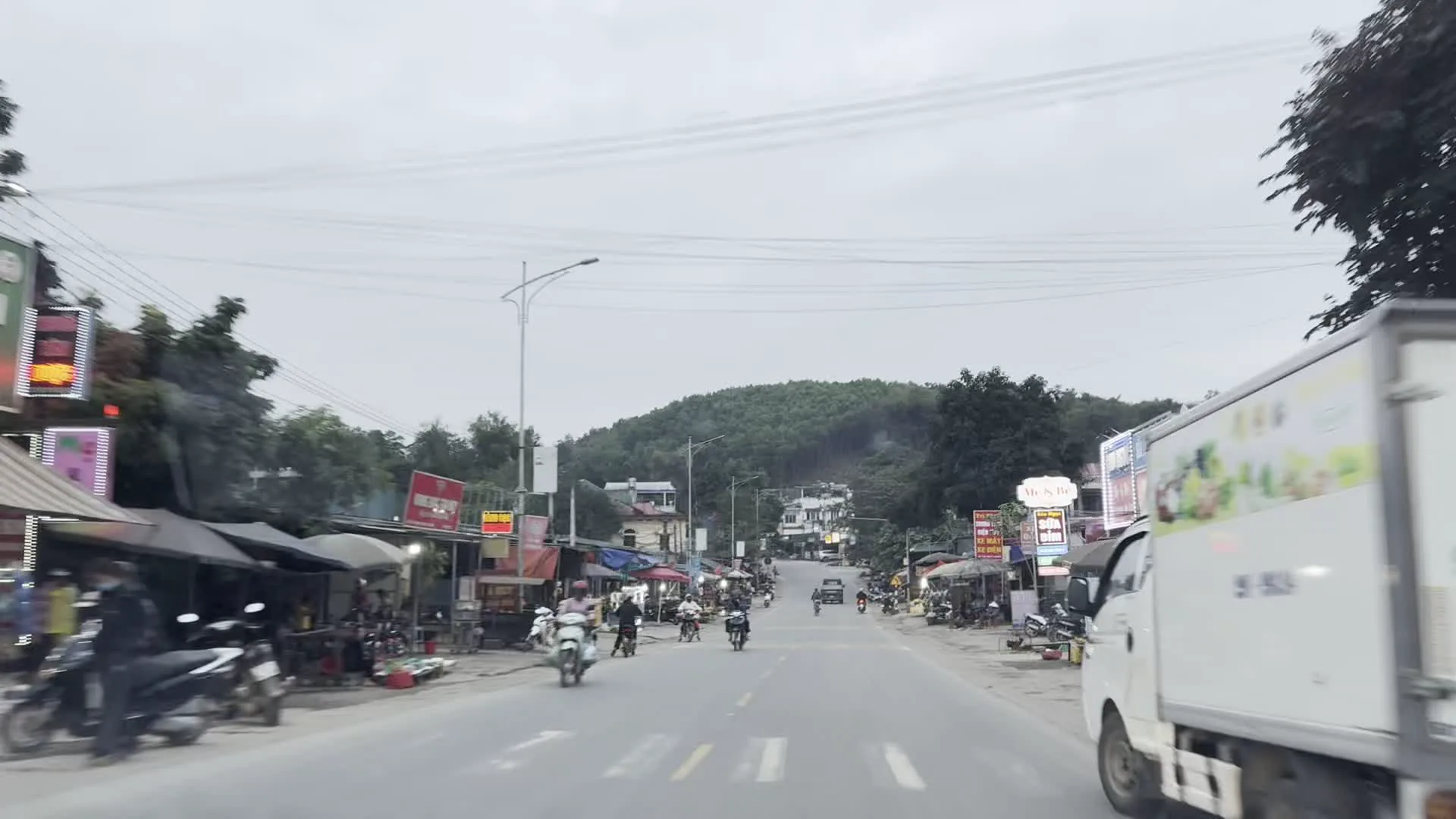 Các hình ảnh ghi lại cảnh quan dọc một con đường ở một khu vực có vẻ là ngoại ô hoặc nông thôn, với những ngọn đồi ở phía sau. Một hình ảnh cho thấy một đoạn đường đông đúc như một thị trấn nhỏ hoặc khu chợ ven đường. Hai bên đường có nhiều cửa hàng, quán ăn, với nhiều người dân địa phương di chuyển bằng xe máy và một chiếc xe tải màu trắng. Có nhiều biển hiệu quảng cáo nhưng chữ viết trên đó bị mờ, khó đọc. Các hình ảnh khác mô tả những đoạn đường vắng vẻ hơn, được bao quanh bởi cây cối xanh tươi, bao gồm cả tre. Có một vài ngôi nhà, ô tô đang lưu thông và một lá cờ Việt Nam được treo bên đường.