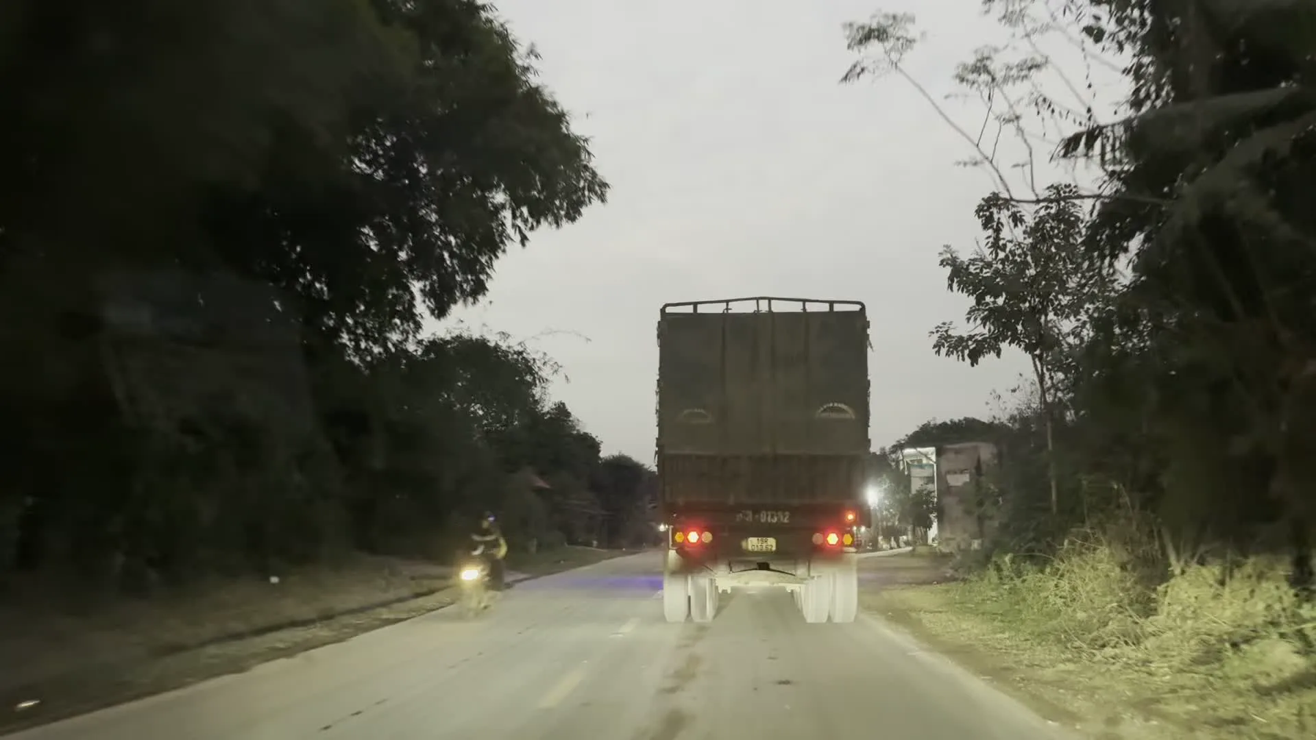 Khung cảnh được ghi lại từ một phương tiện đang di chuyển trên đường vào lúc trời chạng vạng, có thể là sáng sớm hoặc chiều tối. Phía trước là một chiếc xe tải lớn có thùng xe phủ bạt màu sẫm, đang bật đèn hậu. Hai bên đường là cây cối và một vài công trình nhà ở. Có thể thấy một lá cờ đỏ sao vàng của Việt Nam được treo bên đường. Trong một khoảnh khắc, một người đi xe máy xuất hiện ở bên trái. Ở một cảnh khác, một người dường như đang dùng vòi nước tưới ra đường khiến mặt đường bị ướt. Trên đuôi xe tải có chữ nhưng không thể đọc rõ.