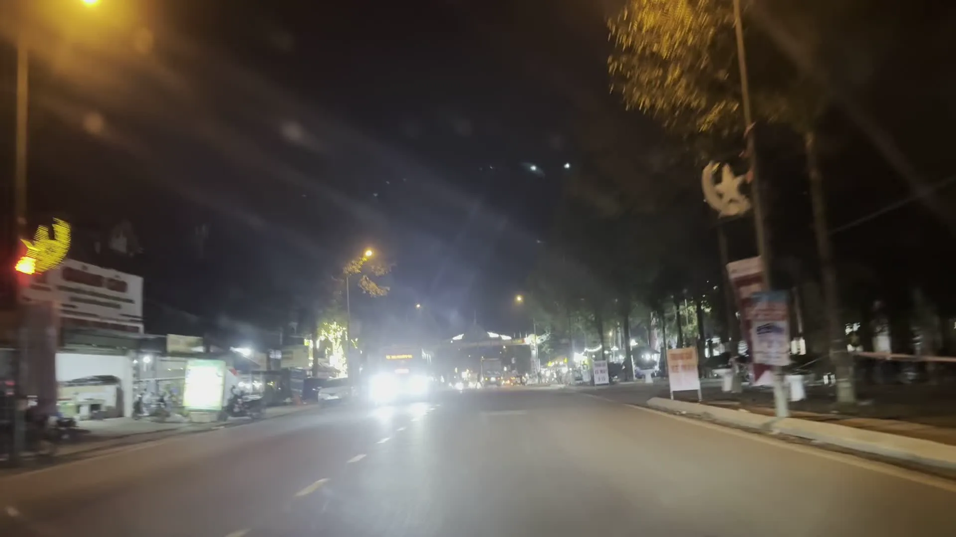 Hình ảnh một con đường ở Việt Nam vào ban đêm, được chụp từ trong một chiếc xe đang di chuyển. Do xe đang chạy và trời tối nên hình ảnh bị mờ và không thể đọc được chữ viết trên các biển hiệu.