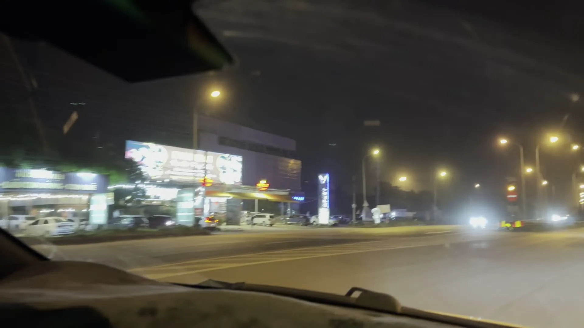 Cảnh quay được ghi lại từ bên trong một chiếc ô tô đang di chuyển trên một con đường lớn có nhiều làn xe vào ban đêm. Con đường được chiếu sáng bởi nhiều cột đèn đường cao áp. Có các phương tiện khác đang lưu thông, bao gồm ô tô, xe tải nhỏ và xe tải lớn. Bên trái đường có một tòa nhà lớn và một trạm xăng đang hoạt động. Phía trên trạm xăng có một tấm biển quảng cáo lớn được chiếu sáng, nhưng nội dung chữ viết trên đó không thể đọc rõ. Một biển báo giao thông hình tròn màu đỏ với vạch ngang màu trắng (biển báo cấm đi) được nhìn thấy ở bên đường.