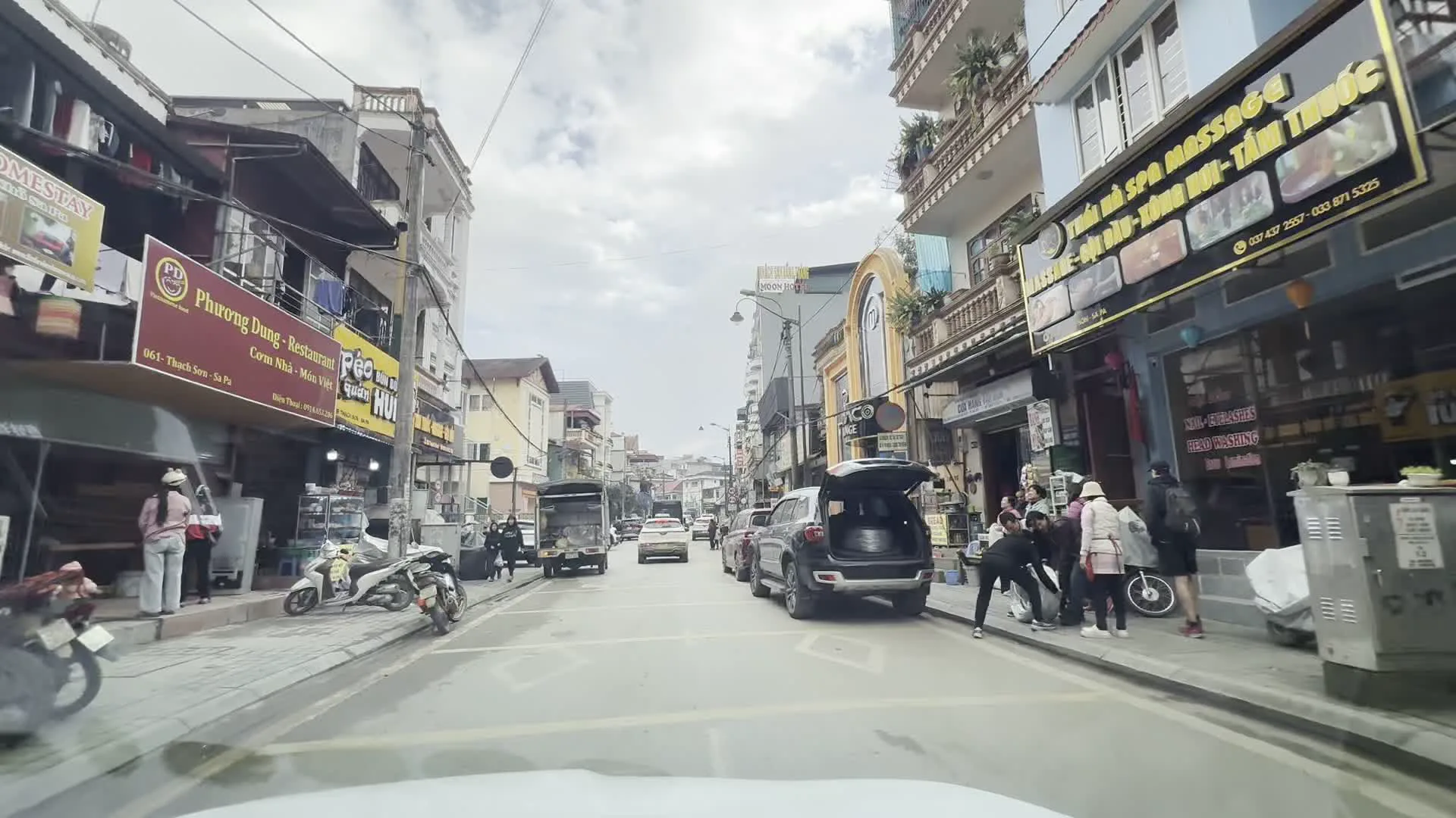 Phố Thạch Sơn, Sa Pa（サパ、タックソン通り）。Biển chỉ dẫn đi Phan Xi Păng, Thác Bạc, Ô Quý Hồ（ファンシーパン山、タックバック滝、オ・クイ・ホー峠方面への案内標識）。Phương Dung - Restaurant（フオン・ズン・レストラン）。MOON HOTEL（ムーンホテル）。Cơm Nhà - Đặc Sản Việt（家庭料理 - ベトナム特産 の看板）。Lẩu Cá Tầm, Cá Hồi（チョウザメとサーモンの鍋料理の看板）