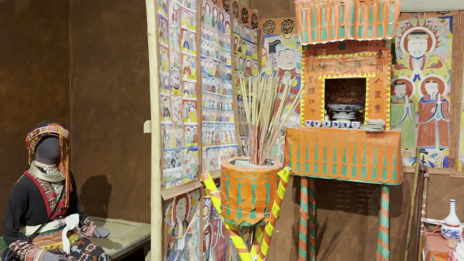 Đây là một không gian trưng bày trong bảo tàng, tái hiện một nghi lễ tín ngưỡng của một dân tộc thiểu số. Cảnh trí bao gồm các ma-nơ-canh mặc trang phục dân tộc truyền thống, được bài trí trong một không gian nghi lễ. Hai ma-nơ-canh ở trung tâm đang diễn tả một nghi lễ, trong đó một người đứng, tay cầm chuông nhỏ và chỉ vào một cuốn sách đang mở có chữ viết (giống chữ Hán hoặc Nôm), người còn lại trong tư thế quỳ hoặc ngồi. Xung quanh có một bàn thờ bằng giấy màu cam, một bát hương lớn cắm đầy nhang, và các bức tường được dán kín bằng nhiều tranh thờ vẽ các nhân vật. Trang phục của các ma-nơ-canh rất cầu kỳ với hoa văn màu đỏ, trắng và khăn đội đầu đặc trưng. Trên sàn nhà có một tấm biển nhỏ ghi: 'KHÔNG ĐƯỢC SỜ VÀO HIỆN VẬT'. Trên bàn thờ và tranh thờ cũng có nhiều chữ viết nhưng không thể đọc rõ.