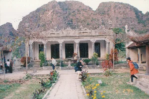 Trên ảnh có dấu ngày tháng màu vàng cam "5 2 '94", tức là ngày 5 tháng 2 năm 1994.。Bức ảnh chụp một khung cảnh thiên nhiên ở vùng nông thôn, có khả năng là tại khu vực Tam Cốc, Ninh Bình. Tiền cảnh là một cánh đồng lúa ngập nước, mặt nước phẳng lặng. Phía sau cánh đồng là những dãy núi đá vôi trùng điệp, đặc trưng của vùng này, đang chìm trong một lớp sương mù dày đặc, tạo nên một không gian mờ ảo và tĩnh lặng. Có thể thấy một vài con chim trắng, có lẽ là cò, ở phía xa trên cánh đồng. Toàn bộ khung cảnh toát lên vẻ yên bình của một vùng quê vào buổi sáng sớm có sương mù.。（日本語訳）。写真にはオレンジ色がかった黄色の「5 2 '94」という日付のスタンプがあり、これは1994年2月5日を意味します。この写真は、おそらくニンビン省タムコック地域の田舎の自然風景を撮影したものです。前景は水に浸かった水田で、水面は穏やかです。水田の後ろには、この地域の特徴である幾重にも連なる石灰岩の山々が濃い霧に沈んでおり、幻想的で静寂な空間を作り出しています。畑の遠くには、おそらくコウノトリかサギと思われる数羽の白い鳥が見えます。風景全体が、霧のかかった早朝の田舎の平和な雰囲気を醸し出しています。