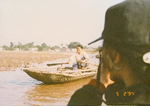 Đây là hình ảnh một cánh đồng lúa rộng lớn ở vùng nông thôn, có thể là khu vực Ninh Bình, vào ngày 5 tháng 2 năm 1994. Các thửa ruộng đã được cày bừa và ngập đầy nước, cho thấy đang trong giai đoạn chuẩn bị gieo cấy cho vụ mùa mới, có khả năng là vụ chiêm xuân. Các bờ ruộng được đắp bằng đất, một số đoạn được kè bằng đá để giữ nước và phân chia các ô ruộng. Xa xa trên cánh đồng là những hàng cột điện chạy dài. Phía chân trời là hình ảnh mờ nhạt của những dãy núi. Không có người hay hoạt động cụ thể nào được ghi lại, nhưng khung cảnh cho thấy công việc đồng áng đang được chuẩn bị. Dưới góc phải của ảnh có dấu ngày tháng "5 2 '94".。（日本語訳）。これは、1994年2月5日の、田舎にある広大な水田の写真で、おそらくニンビン地方のものでしょう。田んぼは耕されて水で満たされており、新しい作付けシーズン、おそらくは春作の作付け準備段階にあることを示しています。畦は土で盛られ、一部は水を保持し田んぼを区切るために石で補強されています。田んぼの遥か向こうには、長く続く電柱の列があります。地平線には、かすかな山々の姿が見えます。人や特定の活動は記録されていませんが、その光景は農作業が準備されていることを示しています。写真の右下には「5 2 '94」という日付のスタンプがあります。