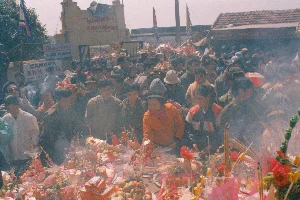 Bức ảnh chụp một bàn thờ bên trong một ngôi đền hoặc chùa, có khả năng là tại khu di tích Chùa Kho, tỉnh Hà Bắc vào năm 1994. Trần nhà được làm bằng phên tre, nứa đan. Trung tâm của bàn thờ là một bức tượng bằng đá trắng, có thể là tượng Bà Chúa Kho, mặc áo gấm sặc sỡ, được thêu hoa văn cầu kỳ. Phía sau tượng, trên bức tường có vách nứa được phủ vải đỏ, có treo một tấm bằng công nhận di tích được đóng khung cẩn thận. Nội dung trên bằng có thể đọc được gồm: "CỘNG HÒA XÃ HỘI CHỦ NGHĨA VIỆT NAM", "BỘ TRƯỞNG BỘ VĂN HÓA", "QUYẾT ĐỊNH", "CÔNG NHẬN DI TÍCH LỊCH SỬ - KIẾN TRÚC NGHỆ THUẬT", và tên di tích có thể là "ĐỀN - ĐÌNH - CHÙA KHO". Xung quanh tượng là các đồ thờ cúng và trang trí. Phía trước có một cành đào lớn đang ra nụ và hoa, được trang trí bằng dây đèn nháy, một hình ảnh đặc trưng của Tết Nguyên Đán ở miền Bắc Việt Nam. Hai bên tượng có các mô hình nhà lầu làm bằng vàng mã (giấy bạc, giấy màu). Ngoài ra còn có một bình hoa loa kèn trắng và hoa hồng giả. Khung cảnh cho thấy không gian thờ tự được trang hoàng cho dịp lễ hội đầu xuân.。（日本語訳）。1994年にハバク省のチュアコー遺跡地区で撮影された可能性のある、寺院または仏塔内部の祭壇を写した写真。天井は編まれた竹や笹のパネルでできている。祭壇の中心には白い石の像があり、それはおそらくバーチュアコー（倉庫の女主人）の像で、精巧な文様が刺繍された色鮮やかな錦の衣装をまとっている。像の後ろ、赤い布で覆われた笹の壁には、丁寧に額装された遺跡認定証が一枚掛けられている。認定証に読み取れる内容には、「ベトナム社会主義共和国」、「文化大臣」、「決定」、「歴史・建築芸術遺跡の認定」、そして遺跡名と思われる「デン（廟）・ディン（亭）・チュア（寺）コー」が含まれる。像の周りには祭祀用品や装飾品がある。前方には、蕾と花をつけた大きな桃の枝が一本あり、点滅する電飾で飾られている。これは北部ベトナムにおけるテト（旧正月）の典型的な光景である。像の両側には、冥器（銀紙、色紙）で作られた高層家屋の模型がある。その他にも、白いユリと造花のバラが入った花瓶がある。この光景は、祭祀空間が早春の祭りのために飾られていることを示している。