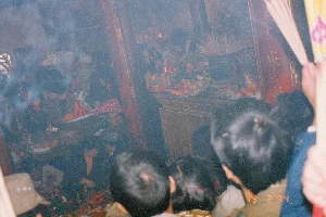 Bức ảnh chụp cảnh bên trong một ngôi chùa hoặc đền, có thể là Chùa Kho ở tỉnh Hà Bắc cũ, vào ngày 19 tháng 2 năm 1994. Không gian rất đông đúc và nghi ngút khói hương. Rất nhiều người dân đang chen chúc nhau để dâng lễ và cầu nguyện trước ban thờ. Ở trung tâm là một ban thờ lớn bằng gỗ, trên đó có một lư hương lớn cắm đầy hương đang cháy. Xung quanh lư hương là rất nhiều mâm lễ vật bao gồm hoa quả, bánh kẹo và các vật phẩm thờ cúng khác. Một số người cũng đang cầm trên tay những mâm lễ. Kiến trúc bên trong nổi bật với các cột gỗ sơn son màu đỏ, trên đó có khắc chữ Hán hoặc chữ Nôm màu vàng nhưng không thể đọc rõ do khói và chất lượng ảnh. Một người ở phía trước bên phải đang cầm một bó hương lớn. Khung cảnh này đặc trưng cho hoạt động đi lễ chùa đầu năm mới Âm lịch của người Việt Nam để cầu may mắn và bình an.。（日本語訳）。1994年2月19日、おそらく旧ハバク省のコー寺と思われる、ある寺院または祠の内部の光景を撮影した写真です。空間は非常に混雑しており、線香の煙が立ち込めています。多くの人々が祭壇の前で供物を捧げ、祈るために押し合っています。中央には大きな木製の祭壇があり、その上には燃えている線香がたくさん立てられた大きな香炉があります。香炉の周りには、果物、菓子、その他の供物を含むたくさんのお供え物の盆があります。何人かの人々も手にお供え物の盆を持っています。右手前の人物が大きな線香の束を持っています。この光景は、幸運と平安を祈るためのベトナム人の旧正月初めの寺参りの活動に特徴的なものです。