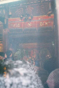 Bức ảnh được chụp vào ngày 19 tháng 2 năm 1994, ghi lại khung cảnh bên trong một ngôi đền hoặc chùa, có khả năng là Chùa Kho ở tỉnh Hà Bắc cũ. Không gian rất đông đúc và có phần mờ ảo do khói hương, cho thấy một buổi lễ đầu năm mới âm lịch. Nhiều người dân đang tập trung, hướng về gian thờ chính để cầu nguyện. Phía trên cao có một bức hoành phi bằng gỗ, khắc nổi ba chữ Hán lớn, có thể đọc từ phải sang trái là "Thánh Mẫu Điện" (殿母聖). Một chiếc đèn chùm kiểu cổ treo ở giữa, ngay phía trước bức hoành phi. Bên dưới là một cửa võng màu đỏ được trang trí với các họa tiết rồng. Gian thờ chính ở phía trong có một pho tượng, có thể là tượng Bà Chúa Kho, mặc trang phục lộng lẫy. Trên ban thờ bày rất nhiều đồ lễ như hoa tươi, nến và hương đang cháy. Khung cảnh thể hiện một hoạt động tín ngưỡng tâm linh đông đúc và trang nghiêm của người dân Việt Nam vào dịp đầu xuân.。（日本語訳）。写真は1994年2月19日に撮影されたもので、ある寺院または祠の内部の光景を記録しており、おそらく旧ハバク省のコー寺（Chùa Kho）であろう。空間は非常に混雑しており、線香の煙でやや霞んでいる様子は、旧正月の初めの儀式であることを示している。多くの人々が集まり、主祭壇に向かって祈りを捧げている。上方には木製の扁額があり、3つの大きな漢字が浮き彫りにされ、右から左に「聖母殿」（Thánh Mẫu Điện、殿母聖）と読める。中央には、扁額のすぐ前に古い様式のシャンデリアが吊るされている。その下には、龍の模様で装飾された赤い門簾（cửa võng）がある。奥の主祭壇には像が一体あり、おそらく豪華な衣装をまとったバー・チュア・コー（Bà Chúa Kho）の像であろう。この光景は、新春の時期におけるベトナムの人々の、混雑しつつも厳かな精神的信仰活動を表している。