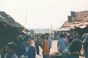 Bức ảnh chụp cận cảnh một tờ giấy giống như một lá sớ cúng, đang được một người cầm trên tay. Tờ giấy được chia thành nhiều cột dọc chứa đầy chữ viết.。1. Thông tin chữ viết:。- Nội dung trên giấy là một bài văn khấn, kết hợp giữa chữ Quốc ngữ in sẵn và chữ viết tay. Các cột chữ được sắp xếp theo kiểu truyền thống.。- Có thể nhận diện một số từ như: "Thiên", "Phật", "Thánh", "Phúc thọ khang ninh", "Việt Nam quốc".。- Ở góc dưới cùng bên phải, có ghi ngày tháng "19 2 '94".。- Ở phía bên trái, có một con dấu lớn hình chữ nhật màu đỏ (ấn triện), bên trong là các ký tự chữ Triện, khó đọc.。- Có những phần chữ viết tay bằng bút mực được thêm vào các cột, ví dụ như trong cột có chữ "Việt Nam quốc".。2. Bối cảnh và Hoạt động:。- Địa điểm: Mặc dù không thấy rõ khung cảnh xung quanh, nhưng dựa vào loại tài liệu này (lá sớ) và bối cảnh được cung cấp (Chùa Kho), có thể suy đoán hoạt động đang diễn ra tại một ngôi chùa hoặc đền thờ.。- Hoạt động: Một người đang cầm lá sớ, có thể là để chuẩn bị cho một buổi lễ cúng hoặc đang xem lại nội dung lời cầu nguyện. Đây là một hoạt động phổ biến của người Việt Nam khi đi lễ chùa đầu năm mới (thời điểm tháng 2) để cầu xin sức khỏe, tài lộc và bình an.。- Vật thể trong ảnh: Đối tượng chính là lá sớ. Ngoài ra còn có một phần cánh tay và bàn tay của người đang cầm sớ, người này có đeo một chiếc đồng hồ.。（日本語訳）。ある人が手に持っている、お供えの願文のような紙を接写した写真。その紙は、文字で埋め尽くされた複数の縦書きの列に分かれています。1. 文字情報：。- 紙の内容は、印刷済みのクオック・グー（ベトナム語アルファベット）と手書き文字を組み合わせた祈祷文です。文字の列は伝統的な様式で配置されています。- 「天」、「仏」、「聖」、「福寿康寧」、「越南国」などのいくつかの単語を認識できます。- 右下隅には、「19 2 '94」という日付が書かれています。- 左側には、大きな長方形の赤い印（印章）があり、その中には判読が難しい篆書体の文字があります。- 例えば「越南国」という文字がある列のように、インクペンによる手書きの部分が各列に追加されています。2. 背景と行動：。- 場所：周囲の風景ははっきりと見えませんが、この種の文書（願文）と提供された背景（コー寺）に基づき、この活動が寺院または祠で行われていると推測できます。- 行動：ある人が願文を手に持っており、おそらく供養の儀式の準備のためか、祈りの言葉の内容を見直しているところでしょう。これは、ベトナム人が新年の初め（2月の時期）に寺院を訪れ、健康、財産、平安を祈願する際の一般的な活動です。- 写真の中の物体：主な対象は願文です。その他に、願文を持っている人の腕と手の一部があり、この人は腕時計をしています。