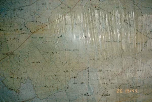 Đây là hình ảnh chụp cận cảnh một tấm bản đồ hành chính cũ của một khu vực thuộc tỉnh Sóc Trăng, được chụp vào năm 1994. Tấm bản đồ giấy đã ngả màu vàng, cho thấy sự cũ kỹ, và được bọc trong một lớp nhựa trong suốt bị nhăn, gây ra nhiều vệt lóa sáng che khuất một phần nội dung.。Loại địa điểm: Đây là một tấm bản đồ hành chính, có thể được treo trên tường hoặc đặt trên bàn trong một văn phòng hoặc cơ quan.。Các vật thể được ghi lại: Tấm bản đồ thể hiện các đường ranh giới hành chính (nét đứt màu đen), một mạng lưới sông ngòi và kênh rạch chằng chịt (đường kẻ màu xanh lam), và một tuyến đường chính (đường kẻ màu đỏ).。Nội dung chữ viết được ghi lại:。Các địa danh có thể đọc được trên bản đồ, chủ yếu là tên các huyện và xã thuộc tỉnh Sóc Trăng:。- Huyện: MỸ XUYÊN, VĨNH CHÂU.。- Xã và các địa danh khác: PHÚ MỸ, ĐẠI TÂM, THAM ĐỒN, MỸ THUẬN, TÀI VĂN, VIÊN AN, VIÊN BÌNH, LÂM KIỆT, THẠNH PHÚ, THANH QUỚI, NGỌC ĐỒNG, THANH THỚI AN, THANH THỚI THUẬN, GIA HÒA 1, GIA HÒA 2, HÒA TÚ, HÒA TÚ 2, NGỌC TỐ, VĨNH HIỆP, HÒA THÀNH, KHÁNH HÒA, HÒA ĐÔNG, LẠC HÒA, LIÊU.。Ở góc dưới bên phải của hình ảnh có một dấu thời gian kỹ thuật số màu cam hiển thị "26 15:43".。（日本語訳）。これは、1994年に撮影された、ソクチャン省のある地域の古い行政地図のクローズアップ写真です。紙の地図は黄ばんでおり、古さを示しています。また、しわの寄った透明なプラスチックの層で覆われており、多くの光の反射を引き起こし、内容の一部を隠しています。場所の種類：これは行政地図であり、事務所や役所の壁に掛けられたり、机の上に置かれたりする可能性があります。記録されている物体：地図には、行政境界線（黒い破線）、複雑に交差する河川や運河の網（青い線）、そして主要な道路（赤い線）が示されています。記録されている文字の内容：。地図上で読み取れる地名、主にソクチャン省に属する県や社の名前：。- 県：MỸ XUYÊN（ミー・スエン）、VĨNH CHÂU（ヴィン・チャウ）。- 社およびその他の地名：PHÚ MỸ, ĐẠI TÂM, THAM ĐỒN, MỸ THUẬN, TÀI VĂN, VIÊN AN, VIÊN BÌNH, LÂM KIỆT, THẠNH PHÚ, THANH QUỚI, NGỌC ĐỒNG, THANH THỚI AN, THANH THỚI THUẬN, GIA HÒA 1, GIA HÒA 2, HÒA TÚ, HÒA TÚ 2, NGỌC TỐ, VĨNH HIỆP, HÒA THÀNH, KHÁNH HÒA, HÒA ĐÔNG, LẠC HÒA, LIÊU。画像の右下隅には、「26 15:43」と表示されたオレンジ色のデジタルタイムスタンプがあります。