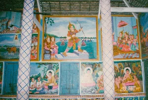 Bối cảnh là bên trong một ngôi chùa, rất có thể là một ngôi chùa Khmer đặc trưng ở khu vực Sóc Trăng, dựa trên phong cách kiến trúc và nghệ thuật. Các bức tường được trang trí dày đặc bằng các bức bích họa (tranh tường) màu sắc rực rỡ, kể lại các câu chuyện trong Phật giáo, có thể là về cuộc đời Đức Phật hoặc các truyện cổ Jataka.。Nổi bật có hai cột trụ tròn lớn được trang trí hoa văn hình thoi màu xanh và trắng. Trần nhà để lộ kết cấu dầm gỗ. Các bức tranh mô tả nhiều cảnh khác nhau: một nhân vật hoàng gia hoặc thần thánh đang giương cung; Đức Phật ngồi thiền hoặc giảng pháp cho các đệ tử; một đám rước với người cầm lọng che. Ngoài ra còn có một cánh cửa gỗ màu xanh lam.。Dưới một số bức tranh có các dòng chữ, chủ yếu là chữ Khmer, ghi lại thông tin nhưng khó đọc chi tiết do chất lượng ảnh. Có thể nhận ra một vài cụm từ như "ភូមិមហានុយបានកសាង" (có thể là ghi công xây dựng) và "ការកើត យាយគ្មាន". Ngoài ra, có cả tên viết bằng ký tự Latin như "STEPHANE EP" và "CELESTER", có thể là tên của những người đã cúng dường cho chùa. Một bức tranh nhỏ phía dưới bên trái có hình hai con trâu và dòng chữ "ver fewន" khó hiểu.。（日本語訳）。背景は寺院の内部で、建築様式や芸術様式から、おそらくソクチャン地方特有のクメール寺院である可能性が非常に高いです。壁は、仏教の物語、おそらくは仏陀の生涯やジャータカ物語を語る、色鮮やかな壁画（壁画）でびっしりと装飾されています。目立つのは、青と白の菱形の模様で装飾された2本の大きな円柱です。天井は木の梁の構造が見えています。絵画はさまざまな場面を描写しています。弓を引く王族または神聖な人物、弟子たちに瞑想または説法をする仏陀、傘を差した人がいる行列などです。さらに、青い木製の扉もあります。いくつかの絵画の下には、主にクメール文字で情報が記録された文字列がありますが、写真の画質のため詳細を読むのは困難です。「ភូមិមហានុយបានកសាង」（おそらく建設の功績を記録したもの）や「ការកើត យាយគ្មាន」といったいくつかのフレーズが認識できます。さらに、「STEPHANE EP」や「CELESTER」といったラテン文字で書かれた名前もあり、これらはおそらく寺に寄進した人々の名前でしょう。左下の小さな絵には、2頭の水牛の絵と、理解しがたい「ver fewន」という文字列があります。