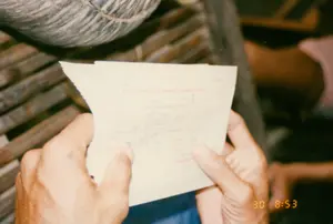 ある人物が領収書を手に持っているのをクローズアップで撮影した写真。領収書には、「現金による農業税徴収領収書」と読める赤い文字が印刷されている。印刷されたものと手書きの両方を含む他の文字は、すべてぼやけていてはっきりと読み取れない。行われている活動は、この人物が証明書、具体的には農業税の納付領収書を確認していることである。この光景は、おそらく農村の家の中であろう、質素な空間を思わせる