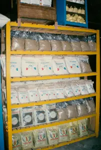 Bức ảnh chụp một kệ sắt màu vàng được sử dụng để trưng bày các sản phẩm thức ăn chăn nuôi, có khả năng là thức ăn cho thủy sản, tại một cửa hàng hoặc nhà kho. Các sản phẩm được đóng gói và sắp xếp ngăn nắp trên các tầng kệ.。Nội dung văn bản trên bao bì sản phẩm:。- Tầng trên cùng: Phía sau kệ có các hộp giấy ghi chữ "Vitamino".。- Tầng thứ hai và thứ ba: Các bao bì màu trắng có in chữ "THỨC ĂN ĐẬM ĐẶC" và logo hình hai con cá.。- Tầng thứ tư: Các bao bì có chữ "THỨC ĂN NUÔI TÔM" và "SỐ 1".。- Tầng dưới cùng: Các bao bì màu vàng nhạt có in chữ "THỨC ĂN NUÔI TÔM", "40% CP", số "1" và tên thương hiệu "KHÁNH HƯNG".。Cảnh vật và hoạt động:。- Địa điểm: Đây là một cửa hàng hoặc kho chứa hàng chuyên bán thức ăn cho ngành nuôi trồng thủy sản, đặc biệt là nuôi tôm và cá, một hoạt động phổ biến ở vùng Sóc Trăng.。- Hoạt động: Các bao thức ăn được trưng bày để bán. Không có người trong ảnh, nhưng bối cảnh cho thấy đây là một hoạt động thương mại.。- Vật thể: Kệ sắt nhiều tầng màu vàng, các loại bao bì thức ăn chăn nuôi (bao giấy, bao nilon) với nhiều nhãn hiệu và chủng loại khác nhau như "Thức ăn đậm đặc" và "Thức ăn nuôi tôm" của thương hiệu "Khánh Hưng".。（日本語訳）。写真は、店舗または倉庫で、飼料製品、おそらくは水産用飼料を陳列するために使用されている黄色い鉄製の棚を写しています。製品は包装され、棚の各段にきちんと整理されています。製品パッケージ上のテキスト内容：。- 最上段：棚の後ろに「Vitamino」と書かれた紙箱があります。- 2段目と3段目：白い袋には「THỨC ĂN ĐẬM ĐẶC」という文字と、2匹の魚の形のロゴが印刷されています。- 4段目：袋には「THỨC ĂN NUÔI TÔM」と「SỐ 1」という文字があります。- 最下段：薄黄色の袋には「THỨC ĂN NUÔI TÔM」、「40% CP」、数字の「1」、そしてブランド名「KHÁNH HƯNG」が印刷されています。風景と活動：。- 場所：これは水産養殖業、特にソクチャン地方で一般的な活動であるエビと魚の養殖用の飼料を専門に販売する店舗または倉庫です。- 活動：飼料の袋が販売用に陳列されています。写真に人はいませんが、背景はこれが商業活動であることを示しています。- 物体：黄色い多層の鉄製棚、ブランド「Khánh Hưng」の「濃縮飼料」や「エビ用飼料」など、多くの異なるブランドや種類を持つ様々な飼料用パッケージ（紙袋、ナイロン袋）。