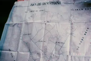 Đây là hình ảnh chụp cận cảnh một tấm bản đồ hành chánh bằng giấy đã cũ và có nhiều nếp gấp, được trải trên một bề mặt có hoa văn caro đỏ trắng, có thể là một tấm khăn trải bàn. Tấm bản đồ thể hiện địa giới hành chính của một khu vực thuộc huyện Mỹ Xuyên, tỉnh Sóc Trăng, với hệ thống sông ngòi và kênh rạch chằng chịt.。Các thông tin văn bản có thể đọc được trên bản đồ bao gồm:。- Tiêu đề: BẢN ĐỒ HÀNH CHÁNH。- Tên huyện: H.MỸ XUYÊN。- Tên các xã: XÃ THẠNH PHÚ, XÃ THAM ĐÔN, XÃ HÒA TÚ 1, XÃ NGỌC ĐÔNG, XÃ GIA (chữ bị cắt).。- Tên các ấp: Ấp HÒA PHƯỚC, Ấp HÒA ĐỨC, Ấp HÒA DĨ, Ấp HÒA NHÂN.。- Tên sông, rạch: SÔNG NHU GIA, Rạch Chùa.。- Dãy số ở góc dưới bên phải: 3 11:41.。Bản đồ sử dụng các đường kẻ màu xanh dương để biểu thị sông ngòi và đường màu đỏ để phân định ranh giới đất đai hoặc địa giới hành chính.。（日本語訳）。これは、古くて多くの折り目がある紙の行政地図のクローズアップ写真で、赤と白のチェック柄の表面、おそらくテーブルクロスの上に広げられています。この地図は、ソクチャン省ミースエン県に属するある地域の行政境界を示しており、川や運河が縦横に張り巡らされています。地図上で読み取れる文字情報は以下の通りです。- タイトル：行政地図 (BẢN ĐỒ HÀNH CHÁNH)。- 県名：ミースエン県 (H.MỸ XUYÊN)。- 社名：タインフー社、タムドン社、ホアトゥー1社、ゴックドン社、ザー社（文字が切れている）。- 邑名：ホアフック邑、ホアドゥック邑、ホアジー邑、ホアニャン邑。- 川、運河名：ニューザー川、チュア運河。- 右下隅の数字列：3 11:41。地図は、川や運河を示すために青い線を使用し、土地の境界または行政境界を区切るために赤い線を使用しています。