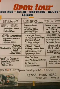 Đây là hình ảnh chụp cận cảnh một tấm biển quảng cáo viết tay cho dịch vụ "Open tour" (tour mở) bằng xe buýt ở Việt Nam, có niên đại khoảng năm 1997. Tấm biển được viết hoàn toàn bằng tiếng Anh, hướng đến đối tượng khách du lịch nước ngoài.。Nội dung chi tiết trên tấm biển như sau:。Tiêu đề chính: "Open tour" màu đỏ.。Lộ trình tổng thể: "FROM HUE -> HOI AN -> NHATRANG -> DA LAT -> SAIGON".。Bảng thông tin được chia thành các cột "ITINERARY" (Lịch trình), "EXCURSION places" (Các điểm tham quan), và "CONTACT OFFICE" (Văn phòng liên hệ).。1.  Chặng "HUE TO HOI AN":。*   Lịch trình: Khởi hành 8:00 sáng hàng ngày, quãng đường 140km trong 6 giờ.。*   Điểm tham quan: Bãi biển Lăng Cô (Langco Beach), Đèo Hải Vân (HaiVan Pass), Bảo tàng Chăm (Cham Museum), Ngũ Hành Sơn (Marble Mountain), Bãi biển Non Nước (China Beach).。*   Văn phòng liên hệ: "Branch office N#3 LE LOI CAF", Tel: 824514, và "SINH CAFÉ".。2.  Chặng "HOI AN TO NHATRANG":。*   Lịch trình: Khởi hành 6:00 sáng hàng ngày, 550km trong 11 giờ.。*   Điểm tham quan: Bãi biển Sa Huỳnh (Sa Huynh Beach), Đèo Cả (Ca pass), Vịnh Sông Cầu (Song Cau Bay), Bãi biển Đại Lãnh (Dai Lanh Beach), Làng chài (Fishing Village).。*   Văn phòng liên hệ: "SINH CAFÉ", khách sạn "Vinh hung Hotel" tại 143 Trần Phú, Hội An, Tel: 861621.。3.  Chặng "NhaTrang To Saigon / Dalat":。*   Lịch trình: Đến Sài Gòn (khởi hành 6:00 sáng, 450km, 9 giờ) hoặc đến Đà Lạt (khởi hành 8:00 sáng, 214km, 6 giờ).。*   Điểm tham quan: Bãi biển Cà Ná (CANA Beach), Tháp Chàm Po Klong Garai ở Phan Rang, Đèo Ngoạn Mục (Ngoan muc Pass).。*   Văn phòng liên hệ: "SINH CAFÉ", khách sạn "MYA Hotel" tại 9 Nguyễn Thiện Thuật, Nha Trang, Tel: 8275...。4.  Chặng "Dalat to Saigon":。*   Lịch trình: Khởi hành 8:00 sáng hàng ngày, 308km trong 6 giờ.。*   Điểm tham quan: Đèo Bảo Lộc (BaoLoc Pass), đồn điền chè và dâu tằm (Tea, Mulbery plantation), Hồ La Ngà (La Nga Lake), nhà nổi (Floating Houses).。*   Văn phòng liên hệ: "SINH CAFÉ", khách sạn "Thanh Van H..." tại 9 Phú Đổng Thiên Vương, Đà Lạt.。Phía dưới cùng của tấm biển có ghi giá vé: "BUS TIKET: 27 USD/person" (Vé xe buýt: 27 đô la Mỹ/người), kèm theo khẩu hiệu "Lowest price but best service" (Giá rẻ nhất nhưng dịch vụ tốt nhất). Có một lời kêu gọi "PLEASE BOOK HERE" (Vui lòng đặt vé tại đây) và một bức ảnh nhỏ chụp một chiếc xe buýt kiểu cũ cùng vài hành khách. Dựa vào chặng đầu tiên bắt đầu từ Huế và địa chỉ liên hệ "N#3 LE LOI CAF", có thể tấm biển này được đặt tại một đại lý du lịch hoặc quán cà phê trên đường Lê Lợi ở thành phố Huế.。（日本語訳）。これは、ベトナムのバスによる「オープントゥール」（自由参加型ツアー）サービスの手書き広告看板のクローズアップ写真で、1997年頃のものです。看板は完全に英語で書かれており、外国人観光客を対象としています。看板の詳細な内容は以下の通りです。メインタイトル：赤色の「Open tour」。全体ルート：「FROM HUE -> HOI AN -> NHATRANG -> DA LAT -> SAIGON」。案内板は「ITINERARY」（旅程）、「EXCURSION places」（観光地）、そして「CONTACT OFFICE」（連絡先オフィス）の列に分かれています。1.  「HUE TO HOI AN」区間：。*   旅程：毎日午前8時出発、距離140kmを6時間。*   観光地：ランコービーチ（Langco Beach）、ハイヴァン峠（HaiVan Pass）、チャム博物館（Cham Museum）、五行山（Marble Mountain）、ノンヌオックビーチ（China Beach）。*   連絡先オフィス：「Branch office N#3 LE LOI CAF」、電話：824514、および「SINH CAFÉ」。2.  「HOI AN TO NHATRANG」区間：。*   旅程：毎日午前6時出発、550kmを11時間。*   観光地：サフィンビーチ（Sa Huynh Beach）、カー峠（Ca pass）、ソンカウ湾（Song Cau Bay）、ダイランビーチ（Dai Lanh Beach）、漁村（Fishing Village）。*   連絡先オフィス：「SINH CAFÉ」、ホイアンのチャンフー通り143番地にある「Vinh hung Hotel」、電話：861621。3.  「NhaTrang To Saigon / Dalat」区間：。*   旅程：サイゴン行き（午前6時出発、450km、9時間）またはダラット行き（午前8時出発、214km、6時間）。*   観光地：カナビーチ（CANA Beach）、ファンランのポー・クロン・ガライ塔、ゴアンムック峠（Ngoan muc Pass）。*   連絡先オフィス：「SINH CAFÉ」、ニャチャンのグエンティエントゥアット通り9番地にある「MYA Hotel」、電話：8275...。4.  「Dalat to Saigon」区間：。*   旅程：毎日午前8時出発、308kmを6時間。*   観光地：バオロック峠（BaoLoc Pass）、茶と桑のプランテーション（Tea, Mulbery plantation）、ラガー湖（La Nga Lake）、水上家屋（Floating Houses）。*   連絡先オフィス：「SINH CAFÉ」、ダラットのフードンティエンヴオン通り9番地にある「Thanh Van H...」ホテル。看板の最下部には料金が記載されています：「BUS TIKET: 27 USD/person」（バスチケット：1人27米ドル）、そして「Lowest price but best service」（最低価格で最高のサービス）というスローガンが添えられています。「PLEASE BOOK HERE」（こちらでご予約ください）という呼びかけと、旧式のバスと数人の乗客を写した小さな写真があります。