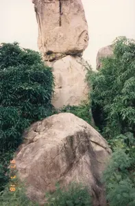 Ở góc dưới bên trái của ảnh có dấu ngày tháng màu cam '97 7 18'. Bức ảnh chụp một cảnh quan thiên nhiên, nổi bật là một cụm đá lớn có hình thù độc đáo. Các tảng đá khổng lồ được xếp chồng lên nhau một cách tự nhiên, tạo nên một khung cảnh ấn tượng và có phần chênh vênh. Xung quanh cụm đá là cây cối và bụi rậm xanh tốt, cho thấy đây là một khu vực có thảm thực vật phong phú. Không có người hay hoạt động của con người trong ảnh. Đây là một cảnh quan thiên nhiên tĩnh lặng, có thể là một địa điểm tham quan nổi tiếng với các khối đá đặc biệt.。（日本語訳）。写真の左下隅に、オレンジ色の日付スタンプ「'97 7 18」があります。この写真は自然の風景を撮影したもので、ユニークな形をした大きな岩の塊が際立っています。巨大な岩々が自然に積み重なり、印象的でやや不安定な光景を作り出しています。岩の塊の周りには青々とした木々や茂みがあり、この地域が豊かな植生を持つことを示しています。写真には人や人間の活動は見られません。これは静かな自然の風景であり、特徴的な岩塊で有名な観光地かもしれません。