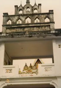 Bức ảnh chụp cận cảnh một cổng chùa Khmer ở Sóc Trăng, thể hiện rõ nét kiến trúc tôn giáo đặc trưng. Cổng chùa được xây dựng thành nhiều tầng. Tầng trên cùng, có màu sẫm do thời gian và phong hóa, được thiết kế với nhiều ô cửa hình vòm, bên trong mỗi ô đặt một bức tượng Phật nhỏ trong tư thế thiền định. Đỉnh cổng được trang trí bằng các ngọn tháp nhọn. Phần thân cổng sơn trắng có một lối đi lớn hình chữ nhật ở giữa. Nhìn xuyên qua cổng, có thể thấy một phần mái của một công trình khác bên trong chùa. Ngay phía trên lối đi là một cụm tượng Phật và các nhân vật tôn giáo được sắp đặt công phu, một số tượng được sơn màu. Toàn bộ công trình kiến trúc trông khá cũ, phản ánh khung cảnh vào thời điểm chụp là ngày 22 tháng 7 năm 1997, như được ghi trên dấu ngày tháng '22 7 '97' ở góc dưới bên trái của ảnh.。（日本語訳）。ソクチャンにあるクメール寺院の門のクローズアップ写真で、特徴的な宗教建築がはっきりと写っている。寺院の門は多層に建てられている。門の頂上は、尖った塔で装飾されている。白く塗られた門の胴体部分には、中央に大きな長方形の通路がある。通路の真上には、精巧に配置された仏陀や宗教的人物の像群があり、いくつかの像には彩色が施されている。建築物全体はかなり古く見え、写真の左下隅にある「'22 7 '97」の日付スタンプに記録されているように、1997年7月22日の撮影時の光景を反映している。