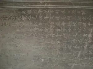 Hình ảnh chụp cận cảnh một tấm bia đá cổ. Bề mặt bia có màu xám, trên đó khắc dày đặc các ký tự chữ Hán theo cột dọc. Các nét chữ đã bị mòn theo thời gian, nhiều phần trở nên mờ và khó đọc. Dựa trên những ký tự còn có thể nhận dạng được như '光順四年...科進士題名' (Quang Thuận tứ niên... khoa Tiến sĩ đề danh), đây có khả năng là một trong những tấm bia Tiến sĩ tại Văn Miếu - Quốc Tử Giám ở Hà Nội, dùng để vinh danh những người đỗ đạt trong các kỳ thi của triều đình xưa. Tấm bia là một hiện vật lịch sử, ghi lại thông tin về khoa cử và nhân tài của đất nước.。（日本語訳）。古い石碑のクローズアップ写真。碑の表面は灰色で、その上には漢字が縦書きでびっしりと刻まれている。文字の線は時間の経過とともに摩耗し、多くの部分がぼやけて読みにくくなっている。「光順四年...科進士題名」（クアン・トゥアン四年...科進士題名）のように、まだ識別できる文字に基づくと、これはハノイの文廟・國子監にある進士碑の一つである可能性があり、昔の朝廷の試験に合格した人々を顕彰するために用いられたものである。この碑は歴史的な遺物であり、国の科挙と有能な人材に関する情報を記録している。