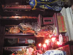 Bức ảnh chụp một bàn thờ trang nghiêm, có khả năng nằm bên trong một ngôi đền hoặc miếu thờ. Trên bàn thờ có một bài vị bằng kim loại màu vàng, khắc chữ đỏ "THÁI HẬU DƯƠNG VÂN NGA". Đây là bàn thờ dành riêng cho Thái hậu Dương Vân Nga. Ở trung tâm là một bức tượng của bà, có thể được làm bằng vật liệu sơn mài hoặc kim loại bóng, đặt trên một bệ thờ bằng gỗ. Phía trước có các vật phẩm thờ cúng, bao gồm một bộ đèn nến điện hình hoa sen đang phát sáng màu đỏ và một lọ hoa bằng sứ men lam trắng có hoa văn rồng, cắm hoa giả màu hồng. Phía trên bàn thờ có treo một tấm vải gấm thêu hoa văn màu xanh và vàng. Khung cảnh cho thấy một không gian thờ cúng, thể hiện sự tôn kính đối với một nhân vật lịch sử.。（日本語訳）。写真は荘厳な祭壇を写しており、おそらく寺院か祠堂の中にあるものだろう。祭壇の上には、金色の金属製の位牌があり、「THÁI HẬU DƯƠNG VÂN NGA」（ズオン・ヴァン・ガー皇太后）という赤い文字が刻まれている。これはズオン・ヴァン・ガー皇太后に捧げられた祭壇である。手前にはお供え物があり、赤く光る蓮の花の形をした一対の電気ろうそく灯と、龍の模様が描かれた青と白の磁器製の花瓶にピンクの造花が生けられている。祭壇の上には、青と黄色の模様が刺繍された錦の布が掛けられている。この光景は、歴史上の人物に対する敬意を表す、礼拝のための空間を示している。