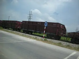 画像には、アスファルト道路と並行に走る線路上で、移動中または停止中の貨物列車が写っている。背景は、後方に緑の田畑と電柱がある農村地域である。列車は、多くの赤褐色の無蓋貨車で構成されている。貨車の車体には、420133、431833、521020のような番号が書かれている。一つの貨車には、「ĐSVN」（ベトナム鉄道）の記号が認識できる。道路沿いには、青い背景に白い矢印がある円形の交通標識があり、「ロータリー交差点」を示している。アスファルトの路面上には、歩行者用または速度を落とすための白い塗装線がある