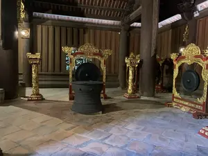 木造建築の内部。中央に大きな太鼓が置かれ、その周囲には赤と金で装飾された枠に吊るされた複数のゴング（銅鑼）が配置されている