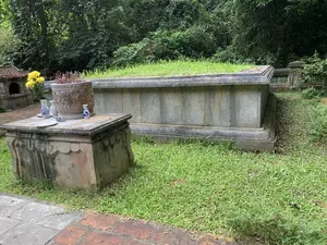 草に覆われた石造りの墳墓と、その手前に花が供えられた供物台