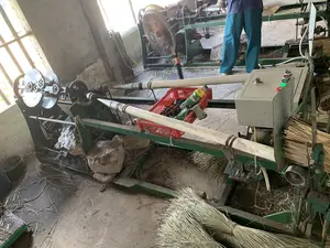 Bối cảnh là một xưởng sản xuất thủ công, có thể là một cơ sở chế biến cói. Một người công nhân mặc quần dài màu xanh lam đang đứng vận hành một cỗ máy phức tạp. Cỗ máy này có màu xanh lá, với nhiều bánh răng và bộ phận cơ khí, dường như được sử dụng để xe hoặc bện các sợi cói khô thành sợi chỉ hoặc dây thừng để dệt chiếu. Xung quanh máy và trên sàn nhà bê tông có rất nhiều bó cói khô, là nguyên liệu sản xuất, và các mảnh vụn cói vương vãi. Bên cạnh máy có một bảng điều khiển với các nút bấm màu đỏ và xanh lá. Ngoài ra, trong xưởng còn có một chiếc quạt điện đang chạy, một chiếc giỏ nhựa màu đỏ đựng một chai nước giải khát có nhãn hiệu "Trà Xanh Không Độ", găng tay và các vật dụng cá nhân khác. Một vài tảng đá lớn được đặt dưới gầm máy, có thể để giữ cho máy ổn định.。（日本語訳）。背景は手工業の作業場で、い草の加工施設かもしれません。青い長ズボンを履いた一人の作業員が、複雑な機械を操作して立っています。この機械は緑色で、多くの歯車や機械部品があり、乾燥したい草の繊維を紡いだり編んだりして、ござを織るための糸やロープにするために使われているようです。機械の周りやコンクリートの床の上には、生産原料である乾燥したい草の束がたくさんあり、い草の破片が散らばっています。機械の隣には、赤と緑の押しボタンが付いた操作盤があります。さらに、作業場には稼働中の扇風機、ブランド名「Trà Xanh Không Độ」の清涼飲料水のボトルが入った赤いプラスチックのかご、手袋、その他の私物があります。機械の下にはいくつかの大きな石が置かれており、機械を安定させるためかもしれません。