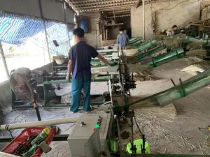 Bối cảnh là một xưởng sản xuất, cụ thể là một xưởng dệt chiếu cói. Có ít nhất ba công nhân (hai nam, một nữ) đang làm việc. Hoạt động chính là vận hành một dàn máy dệt chiếu công nghiệp hoặc bán tự động. Các công nhân đang đưa các sợi cói khô vào máy để dệt thành chiếu. Rất nhiều sợi cói và sản phẩm chiếu đang dệt có thể được nhìn thấy trên các máy và trên sàn nhà. Các vật thể khác trong xưởng bao gồm một chiếc quạt điện, một bảng điều khiển máy có các nút bấm, các bó sợi cói nguyên liệu, và một giỏ nhựa màu đỏ. Không gian xưởng có kết cấu đơn giản với mái lợp, tường gạch và sàn xi măng.。（日本語訳）。背景は生産工場、具体的にはい草のござを織る工場です。少なくとも3人の労働者（男性2人、女性1人）が働いています。主な活動は、工業用または半自動のござ織り機を操作することです。労働者たちは、ござを織るために乾燥したい草の繊維を機械に入れています。機械の上や床の上には、たくさんのい草の繊維と織られているござ製品が見られます。工場内にあるその他の物には、扇風機、押しボタン付きの機械操作パネル、原料のい草の繊維の束、そして赤いプラスチック製の籠が含まれます。工場の空間は、屋根、レンガの壁、セメントの床というシンプルな構造です。