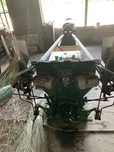 Bức ảnh chụp một cỗ máy công nghiệp lớn màu xanh lá cây trong một nhà xưởng hoặc kho. Đây là máy dùng để sản xuất dây thừng từ sợi thực vật, có thể là cói, dựa trên các bó nguyên liệu khô được đặt trên máy và rơi vãi trên sàn nhà bê tông. Trên thân máy có một bảng điều khiển với nút bấm màu đỏ, đèn xanh và công tắc. Ngoài ra còn có một tấm biển kim loại ghi thông số kỹ thuật bằng chữ Trung Quốc, nội dung có thể đọc được bao gồm:。- GZY鑫盛全自动草绳编织机械设备 (Thiết bị máy dệt dây cỏ hoàn toàn tự động GZY Xinsheng)。- 寿县振宇农机销售有限公司 (Công ty TNHH kinh doanh máy nông nghiệp Zhenyu, huyện Thọ)。- Biển cảnh báo điện giật hình tam giác màu vàng với dòng chữ "当心触电" (Cẩn thận điện giật).。Không gian xung quanh là một nhà xưởng với tường bê tông, phía sau có một chiếc quạt điện.。（日本語訳）。写真は、工場または倉庫の中にある、一台の大きな緑色の産業機械を写しています。これは、機械の上に置かれ、コンクリートの床に散らばっている乾燥した原料の束から判断して、おそらくイグサなどの植物繊維からロープを製造するための機械です。機械本体には、赤い押しボタン、緑のランプ、スイッチが付いたコントロールパネルがあります。その他に、中国語で技術仕様が書かれた金属製のプレートもあり、読み取れる内容には以下が含まれます：。- GZY鑫盛全自动草绳编织机械设备（GZY Xinsheng 全自動草ロープ編み機）。- 寿县振宇农机销售有限公司（寿県Zhenyu農業機械販売有限会社）。- 「当心触电」（感電注意）という文字が入った、黄色い三角形の感電警告表示。周囲の空間はコンクリートの壁の工場で、後ろには扇風機があります。