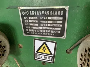 Hình ảnh chụp cận cảnh một tấm biển thông số kỹ thuật bằng kim loại và một nhãn cảnh báo được gắn trên một cỗ máy công nghiệp màu xanh lá cây. Đây là một máy dệt dây rơm tự động.。Nội dung chi tiết trên tấm biển bằng tiếng Trung được ghi lại như sau:。- Tên thiết bị: GZY 鑫盛全自动草绳编织机械设备 (Thiết bị máy dệt dây rơm hoàn toàn tự động GZY Xinsheng)。- Kiểu máy (型号): GZY-28898。- Số xuất xưởng (出厂编号): 8888-5007。- Công suất (功率): 1.48KW。- Trọng lượng máy (机器重量): 300KG。- Điện áp (电压): 220V。- Ngày xuất xưởng (出厂日期): 2024-01-08。- Kích thước bên ngoài (外型尺寸): Dài 270CM, Rộng 110CM, Cao 110CM。- Công ty bán hàng: 寿县振宇农机销售有限公司 (Công ty TNHH kinh doanh máy nông nghiệp Zhenyu, huyện Thọ)。- Địa chỉ: 安徽省淮南市寿县板桥镇工业园 (Khu công nghiệp thị trấn Bản Kiều, huyện Thọ, thành phố Hoài Nam, tỉnh An Huy, Trung Quốc)。Bên dưới là một nhãn cảnh báo hình chữ nhật với biểu tượng tia sét trong hình tam giác màu vàng và dòng chữ '当心触电', có nghĩa là 'Cẩn thận điện giật'.。Bối cảnh cho thấy đây là một máy móc được sử dụng trong sản xuất nông nghiệp hoặc thủ công nghiệp, cụ thể là để dệt dây từ vật liệu như rơm hoặc cói. Với thông tin địa lý 'Ngason', một khu vực nổi tiếng với nghề dệt cói ở Việt Nam, có khả năng chiếc máy này được sử dụng tại một cơ sở sản xuất ở đó.。（日本語訳）。緑色の産業機械に取り付けられた金属製の仕様銘板と警告ラベルのクローズアップ写真。これは自動わら縄編み機である。銘板の中国語による詳細な内容は以下の通りである：。- 設備名：GZY 鑫盛全自动草绳编织机械设备 (GZY Xinsheng 全自動わら縄編み機械設備)。- 型番 (型号): GZY-28898。- 製造番号 (出厂编号): 8888-5007。- 出力 (功率): 1.48KW。- 機械重量 (机器重量): 300KG。- 電圧 (电压): 220V。- 製造年月日 (出厂日期): 2024-01-08。- 外形寸法 (外型尺寸): 長さ270CM、幅110CM、高さ110CM。- 販売会社：寿县振宇农机销售有限公司 (寿県Zhenyu農機販売有限会社)。- 住所：安徽省淮南市寿县板桥镇工业园 (中国安徽省淮南市寿県板橋鎮工業団地)。その下には、黄色の三角形の中に稲妻のシンボルと「当心触电」という文字が書かれた長方形の警告ラベルがあり、「感電注意」を意味する。背景から、これが農業または手工業生産、具体的にはわらやい草のような材料から縄を編むために使用される機械であることがわかる。ベトナムでい草織りの産地として有名な「ガソン」という地理情報から、この機械がそこの生産施設で使用されている可能性がある。