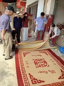 Bối cảnh diễn ra tại một cửa hàng hoặc xưởng sản xuất chiếu cói, có thể là ở Nga Sơn. Một nhóm người gồm cả nam và nữ đang tụ tập xem một chiếc chiếu lớn được trải trên sàn xi măng. Một người phụ nữ lớn tuổi, có vẻ là người bán hàng, đang giới thiệu sản phẩm cho các khách hàng bằng cách lật một góc chiếu lên. Các khách hàng đang chăm chú quan sát chất lượng và hoa văn của chiếu. Chiếc chiếu cói có màu tự nhiên với viền và các họa tiết trang trí màu đỏ. Trên chiếu có dệt rõ dòng chữ "Nga Sơn" và "Kỷ Niệm", cùng với một ký tự Nôm hoặc chữ Hán lớn được cách điệu ở trung tâm. Ở hậu cảnh, có rất nhiều cuộn chiếu khác được dựng đứng và xếp chồng lên nhau, một số được bọc trong túi ni lông, cho thấy đây là một cơ sở chuyên kinh doanh mặt hàng này.。（日本語訳）。舞台は、い草のござの店または工房で、おそらくガソン（Nga Sơn）にあります。男女を含む一団の人々が、セメントの床に広げられた大きなござを囲んで見ています。店員と思われる年配の女性が、ござの角をめくり上げて客たちに商品を説明しています。客たちは、ござの品質と模様を熱心に観察しています。そのい草のござは自然な色合いで、縁と装飾模様は赤色です。ござには「Nga Sơn」と「Kỷ Niệm」（記念）という文字がはっきりと織り込まれており、中央にはデザイン化された大きなチュノムまたは漢字一文字があります。背景には、他の多くの巻かれたござが立てられたり積み重ねられたりしており、いくつかはビニール袋に包まれています。このことから、ここがこの商品を専門に扱う施設であることがわかります。