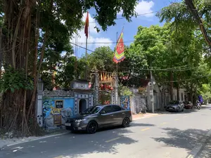 Bối cảnh là một con đường vào một ngày nắng, có cây cối xanh tươi hai bên. Bên lề đường là cổng vào một công trình kiến trúc cổ, được xác định là Đình Đệ Nhị qua tấm biển "ĐÌNH ĐỆ NHỊ NĂM 1836". Đây là một ngôi đình làng, một loại hình kiến trúc tín ngưỡng cộng đồng truyền thống ở Việt Nam. Cổng đình được xây dựng công phu với mái cong, các họa tiết trang trí và câu đối chữ Hán ở hai bên cột. Trên tường bên cạnh cổng có một bức phù điêu lớn hình con voi. Gần đó có một tấm bia đá nhỏ khắc chữ Hán "下馬" (Hạ Mã), có nghĩa là "xuống ngựa", một biển báo truyền thống yêu cầu thể hiện sự tôn kính. Phía trên cổng có treo cờ Tổ quốc Việt Nam và cờ hội ngũ sắc có hình rồng. Một chiếc ô tô màu xám đang đỗ sát lề đường ngay trước cổng đình. Khung cảnh chung khá yên tĩnh, không có hoạt động lễ hội hay mua bán nào diễn ra.。（日本語訳）。背景は晴れた日の一本の道で、両側には青々とした木々があります。道端には古い建築物への門があり、「ĐÌNH ĐỆ NHỊ NĂM 1836」という看板によってĐệ Nhị亭と特定されています。これは村の亭（ディン）であり、ベトナムにおける伝統的な共同体の信仰建築の一種です。亭の門は、湾曲した屋根、装飾的な模様、そして両側の柱にある漢文の対聯（ついれん）で精巧に建てられています。門の隣の壁には、象の形をした大きなレリーフがあります。その近くには、漢文で「下馬」（Hạ Mã）と刻まれた小さな石碑があり、これは「馬から降りよ」という意味で、敬意を表すことを要求する伝統的な標識です。門の上にはベトナムの国旗と、龍が描かれた五色の祭りの旗が掲げられています。一台の灰色の自動車が、亭の門のすぐ前の道端に駐車しています。全体的な光景はかなり静かで、祭りや商売などの活動は行われていません。