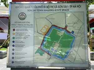 Đây là hình ảnh một tấm biển thông tin lớn, có khung kim loại sáng bóng, được đặt ngoài trời tại một khu vực công cộng. Tấm biển cung cấp thông tin chi tiết về "KHÔNG GIAN TUYẾN PHỐ ĐI BỘ THỊ XÃ SƠN TÂY - TP HÀ NỘI", với bản dịch tiếng Anh là "SON TAY TOWN WALKING ROUTE SPACE".。Nội dung trên biển bao gồm:。1.  **Chữ viết:**。*   **Tiêu đề:** KHÔNG GIAN TUYẾN PHỐ ĐI BỘ THỊ XÃ SƠN TÂY - TP HÀ NỘI.。*   **Thời gian hoạt động:** 18h00 Thứ 7 ÷ 12h00 Chủ nhật (Hàng tuần).。*   **Các khu vực hoạt động:**。*   1. Không gian đi bộ, bán đồ lưu niệm, giải khát.。*   2. Không gian tổ chức sự kiện văn hóa, Vui chơi, nghệ thuật đường phố.。*   3. Không gian ẩm thực xứ Đoài, Chợ hoa.。*   **Các điểm đỗ xe:** Liệt kê các điểm đỗ xe tại phố Trần Hưng Đạo, phố Phùng Hưng, phố Lê Lợi, khu Vườn hoa Trung tâm, Hội trường Tây Đô, và phố Phó Đức Chính.。2.  **Tình景 và vật thể:**。*   **Địa điểm:** Một tấm biển chỉ dẫn công cộng, có thể đặt ở lối vào hoặc bên trong khu phố đi bộ Sơn Tây.。*   **Hoạt động:** Tấm biển đang thực hiện chức năng cung cấp thông tin và bản đồ cho du khách và người dân địa phương về khu phố đi bộ.。*   **Vật thể:**。*   **Bản đồ:** Một bản đồ chi tiết chiếm phần lớn diện tích biển báo, thể hiện rõ các tuyến phố đi bộ (Tuyến phố Phùng Hưng, Trần Hưng Đạo, Lê Lợi, Phó Đức Chính), các địa danh nổi bật như Thành cổ Sơn Tây, Hào nước Thành cổ, Điện Kính Thiên, Nhà thi đấu, Trung tâm VHTT Sơn Tây, Trụ sở HĐND-UBND Thị xã Sơn Tây. Có một ký hiệu "BẠN ĐANG Ở ĐÂY" để xác định vị trí người xem.。*   **Logo:** Logo của Sơn Tây được in nổi bật.。*   **Phản chiếu:** Bề mặt bóng của biển báo phản chiếu hình ảnh người chụp ảnh, cây cối và bầu trời, cho thấy đây là một cảnh chụp ngoài trời vào ban ngày.。（日本語訳）。これは、公共の場所に屋外設置された、光沢のある金属フレームを持つ大きな案内板の写真です。この案内板は、「ソンタイ市社－ハノイ市 歩行者天国空間」に関する詳細な情報を提供しており、英語訳は「SON TAY TOWN WALKING ROUTE SPACE」です。案内板の内容は以下の通りです：。1.  **文字情報：**。*   **タイトル：** ソンタイ市社－ハノイ市 歩行者天国空間。*   **活動時間：** 毎週土曜日18時00分から日曜日12時00分まで。*   **活動エリア：**。*   1. 歩行者、土産物販売、飲料のスペース。*   2. 文化イベント、娯楽、ストリートアート開催のスペース。*   3. ドアイ地方のグルメ、花市場のスペース。*   **駐車場：** チャン・フン・ダオ通り、フン・フン通り、レ・ロイ通り、中央フラワーガーデンエリア、タイドー会館、フォー・ドゥック・チン通りの駐車場がリストアップされています。2.  **情景と物体：**。*   **活動：** 案内板は、観光客や地元住民に歩行者天国に関する情報と地図を提供する機能を果たしています。*   **物体：**。*   **地図：** 案内板の大部分を占める詳細な地図で、歩行者天国となる通り（フン・フン通り、チャン・フン・ダオ通り、レ・ロイ通り、フォー・ドゥック・チン通り）、ソンタイ古城、古城の堀、キンティエン殿、体育館、ソンタイ文化情報センター、ソンタイ市社人民評議会・人民委員会庁舎などの有名なランドマークが明確に示されています。「現在地」を示す記号があり、見る人の位置を特定できます。*   **ロゴ：** ソンタイのロゴが目立つように印刷されています。*   **反射：** 案内板の光沢のある表面には、撮影者、木々、空が映り込んでおり、これが日中の屋外で撮影されたシーンであることを示しています。
