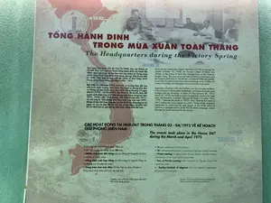 Đây là hình ảnh một tấm bảng thông tin tại một khu di tích hoặc bảo tàng, có nội dung bằng cả tiếng Việt và tiếng Anh, mô tả về Tổng hành dinh trong chiến dịch Mùa Xuân 1975.。**Nội dung chữ viết được ghi lại như sau:**。**Tiêu đề chính:** TỔNG HÀNH DINH TRONG MÙA XUÂN TOÀN THẮNG.。**Đoạn văn thứ nhất:**。'Sau ngày tiếp quản Thủ đô (10/10/1954), khu vực Thành cổ Hà Nội được lựa chọn trở thành Tổng Hành dinh của Quân đội Nhân dân Việt Nam, là nơi làm việc của Quân ủy Trung ương và Bộ Tổng Tham mưu (Khu A Bộ Quốc phòng). Đây là nơi diễn ra nhiều cuộc họp cơ mật của Bộ Chính trị Ban Chấp hành Trung ương Đảng trong giai đoạn 1954 - 1975.。Đặc biệt, từ cuối năm 1974, nắm bắt xu hướng thay đổi của tình hình chiến trường miền Nam, Bộ Chính trị đã kịp thời đưa ra những chỉ đạo chiến lược, then chốt. Trong khoảng 75 ngày (08/01/1975 - 25/03/1975), Bộ Chính trị đã ba lần thay đổi quyết sách chiến lược từ: “Giải phóng miền Nam trong hai năm 1975 - 1976”; đến “Giải phóng miền Nam trong năm 1975”; và cuối cùng là “Giải phóng miền Nam trước mùa mưa năm 1975”. Những chỉ đạo linh hoạt, sáng tạo, kịp thời đó đã huy động tổng lực sức người, sức của của toàn dân tộc, làm nên sự toàn thắng của Chiến dịch Hồ Chí Minh lịch sử, giải phóng miền Nam, thống nhất đất nước.'。**Tiêu đề thứ hai:** CÁC HOẠT ĐỘNG TẠI NHÀ D67 TRONG THÁNG 03 - 04/1975 VỀ KẾ HOẠCH GIẢI PHÓNG MIỀN NAM.。**Danh sách các hoạt động:**。*   Hội nghị Bộ Chính trị mở rộng: 13 cuộc。*   Hội nghị Quân ủy Trung ương: 06 cuộc。*   Nhiều cuộc trao đổi riêng của các đồng chí trong Bộ Chính trị và Quân ủy Trung ương。*   Hàng chục cuộc họp riêng của Đại tướng Võ Nguyên Giáp với Tổ thường trực chỉ đạo tác chiến。*   Hàng trăm bức mật điện chỉ đạo liên tục được chuyển từ Tổng Hành dinh (Nhà D67) tới các mặt trận。**Nguồn:** (Nguồn: Hồ sơ Di tích cách mạng Nhà D67 - Khu A Bộ Quốc phòng)。**Mô tả cảnh vật và hoạt động:**。*   **Loại địa điểm:** Đây là một tấm bảng thông tin trưng bày, có thể nằm trong một bảo tàng hoặc khu di tích lịch sử như Hoàng thành Thăng Long, dựa trên nội dung đề cập đến Nhà D67 và Thành cổ Hà Nội.。*   **Vật thể:** Tấm bảng có nền màu be, chữ màu đỏ và đen. Trên bảng có in hình bản đồ Việt Nam màu đỏ, đánh dấu các địa điểm HÀ NỘI, QUẦN ĐẢO HOÀNG SA, QUẦN ĐẢO TRƯỜNG SA. Phía trên là một bức ảnh tư liệu đen trắng chụp cảnh một cuộc họp, trong đó có nhiều người đàn ông đang ngồi quanh bàn họp.。*   **Hoạt động:** Tấm bảng mô tả các hoạt động lịch sử quan trọng diễn ra tại Tổng Hành dinh (Nhà D67) vào năm 1975, bao gồm các cuộc họp của Bộ Chính trị, Quân ủy Trung ương và các chỉ đạo chiến lược cho chiến dịch giải phóng miền Nam. Bức ảnh trên bảng cho thấy một cuộc họp đang diễn ra.。（日本語訳）。これは、史跡または博物館にある案内板の画像です。ベトナム語と英語の両方で書かれており、1975年春の作戦における総司令部について説明しています。**記載されている文字の内容は以下の通りです：**。**主見出し：**完全勝利の春における総司令部。**第一段落：**。「首都接収の日（1954年10月10日）の後、ハノイ城址地区はベトナム人民軍の総司令部となるべく選ばれ、中央軍事委員会と参謀本部（国防省A地区）の執務場所となりました。ここは1954年から1975年の期間において、党中央執行委員会政治局の多くの機密会議が行われた場所です。特に、1974年末から、南部戦場の状況の変化の傾向を捉え、政治局は適時に戦略的かつ重要な指示を出しました。約75日間（1975年1月8日～1975年3月25日）のうちに、政治局は戦略的決定を3回変更しました。「1975年～1976年の2年間で南部を解放する」から、「1975年内に南部を解放する」へ、そして最終的には「1975年の雨季前に南部を解放する」となりました。これらの柔軟で創造的、かつ適時な指示は、全民族の人的・物的資源を総動員し、歴史的なホーチミン作戦の完全勝利、南部解放、国家統一を成し遂げました。」。**第二見出し：**南部解放計画に関する1975年3月～4月のD67庁舎における活動。**活動リスト：**。*   拡大政治局会議：13回。*   中央軍事委員会会議：6回。*   政治局および中央軍事委員会の同志による多くの個別意見交換。*   ヴォー・グエン・ザップ大将と作戦指導常任班との数十回の個別会議。*   総司令部（D67庁舎）から各戦線へ数百通の機密指令電報が継続的に送付された。**出典：**（出典：D67庁舎革命史跡資料 - 国防省A地区）。**風景と活動の説明：**。*   **場所の種類：**これは展示されている案内板であり、D67庁舎とハノイ城址に関する内容から、タンロン皇城のような博物館または歴史的遺跡地区にある可能性があります。*   **物体：**案内板はベージュ色の背景に、赤と黒の文字があります。板上には赤いベトナム地図が印刷され、ハノイ、ホアンサ諸島（パラセル諸島）、チュオンサ諸島（スプラトリー諸島）の地点が記されています。上部には、会議の様子を写した白黒の資料写真があり、多くの男性が会議テーブルを囲んで座っています。*   **活動：**案内板は、1975年に総司令部（D67庁舎）で行われた重要な歴史的活動を説明しており、それには政治局、中央軍事委員会の会議、および南部解放作戦のための戦略的指示が含まれます。板上の写真は会議が行われている様子を示しています。