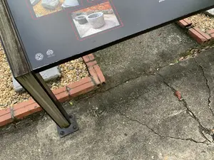 Bức ảnh chụp một tấm biển thông tin tại khu di tích Hoàng thành Thăng Long. Trên tấm biển màu đen có các dòng chữ và logo: logo Di sản Thế giới của UNESCO với các chữ 'WORLD HERITAGE', 'PATRIMOINE MONDIAL', 'PATRIMONIO MUNDIAL' và logo cùng dòng chữ 'HOÀNG THÀNH THĂNG LONG'. Một phần chữ khác ở góc trên bên phải có vẻ như là '...phố bi...' nhưng không thể đọc rõ. Tấm biển còn có hình ảnh chụp các hiện vật bằng đá, trông giống như những chiếc cối đá. Biển được đặt trên một trụ đỡ bằng gỗ và kim loại. Phía dưới là nền bê tông bị nứt và một khu vực nhỏ rải sỏi được bao quanh bởi gạch đỏ.。（日本語訳）。タンロン皇城遺跡地区にある案内板を撮影した写真です。黒い看板には、「WORLD HERITAGE」、「PATRIMOINE MONDIAL」、「PATRIMONIO MUNDIAL」の文字が入ったUNESCO世界遺産のロゴと、「HOÀNG THÀNH THĂNG LONG」という文字が入ったロゴがあります。右上隅にある別の文字の一部は「...phố bi...」のようですが、はっきりと読むことはできません。看板は木製と金属製の支柱の上に設置されています。下にはひびの入ったコンクリートの地面と、赤レンガで囲まれた砂利敷きの小さなエリアがあります。