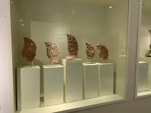 Bên trong một tủ kính trưng bày của bảo tàng, có năm hiện vật khảo cổ bằng đất nung được đặt trên các bệ đỡ màu trắng có chiều cao khác nhau. Các hiện vật này là ngói trang trí diềm mái, được chạm khắc tinh xảo với các họa tiết linh vật (có thể là rồng hoặc phượng). Phía sau các hiện vật có một bảng thông tin, mặc dù chữ bị ngược và khó đọc, nhưng có thể nhận ra các dòng chữ: "NGÓI UYÊN ƯƠNG", "MANDARIN DUCK TILES", và "Đất nung, thế kỷ 15-17". Khung cảnh cho thấy đây là một không gian trưng bày hiện vật lịch sử, có ánh sáng chiếu vào để làm nổi bật các chi tiết của cổ vật.。（日本語訳）。博物館の展示ガラスケースの中に、5つのテラコッタ製の考古学的遺物が、高さの異なる白い台座の上に置かれています。これらの遺物は軒先を飾る瓦で、霊獣（龍または鳳凰の可能性あり）の文様が精巧に彫刻されています。遺物の後ろには案内板があり、文字は逆さで読みにくいですが、「NGÓI UYÊN ƯƠNG」、「MANDARIN DUCK TILES」、そして「テラコッタ、15～17世紀」という文字が認識できます。この光景は、ここが歴史的遺物を展示する空間であることを示しており、古代遺物の細部を際立たせるために照明が当てられています。